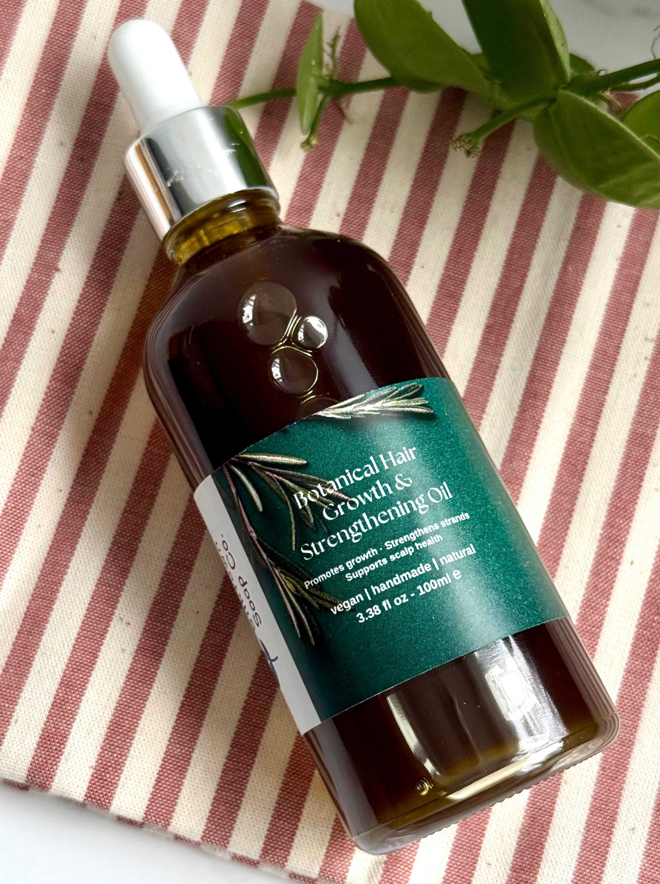 Botanical hair growth oil bottle on a striped fabric background