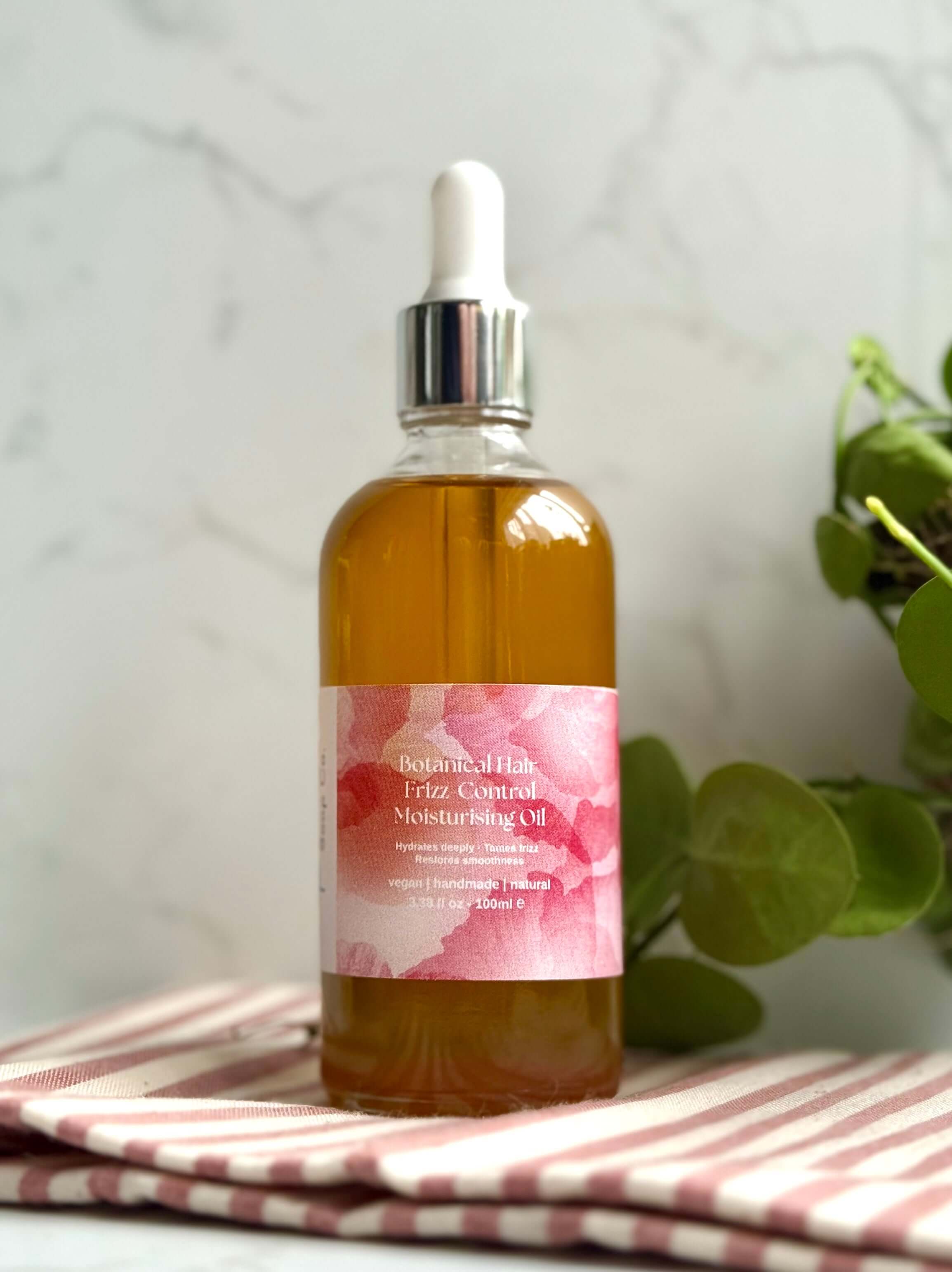 Bottle of hair oil with a pink label on a striped cloth