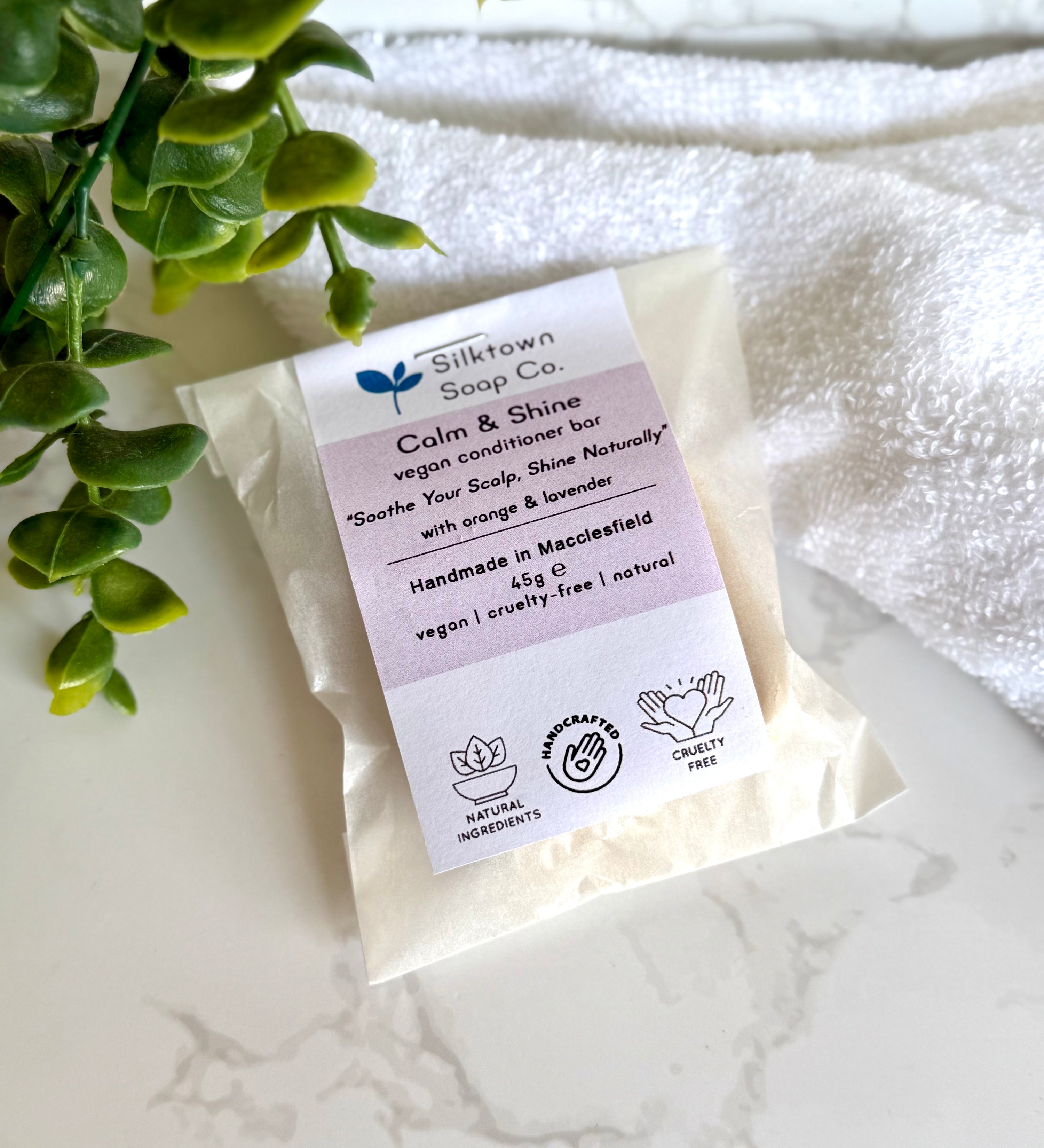 Calm & Shine Natural Haircare Conditioner Bar oin packaging with a towel and foliage