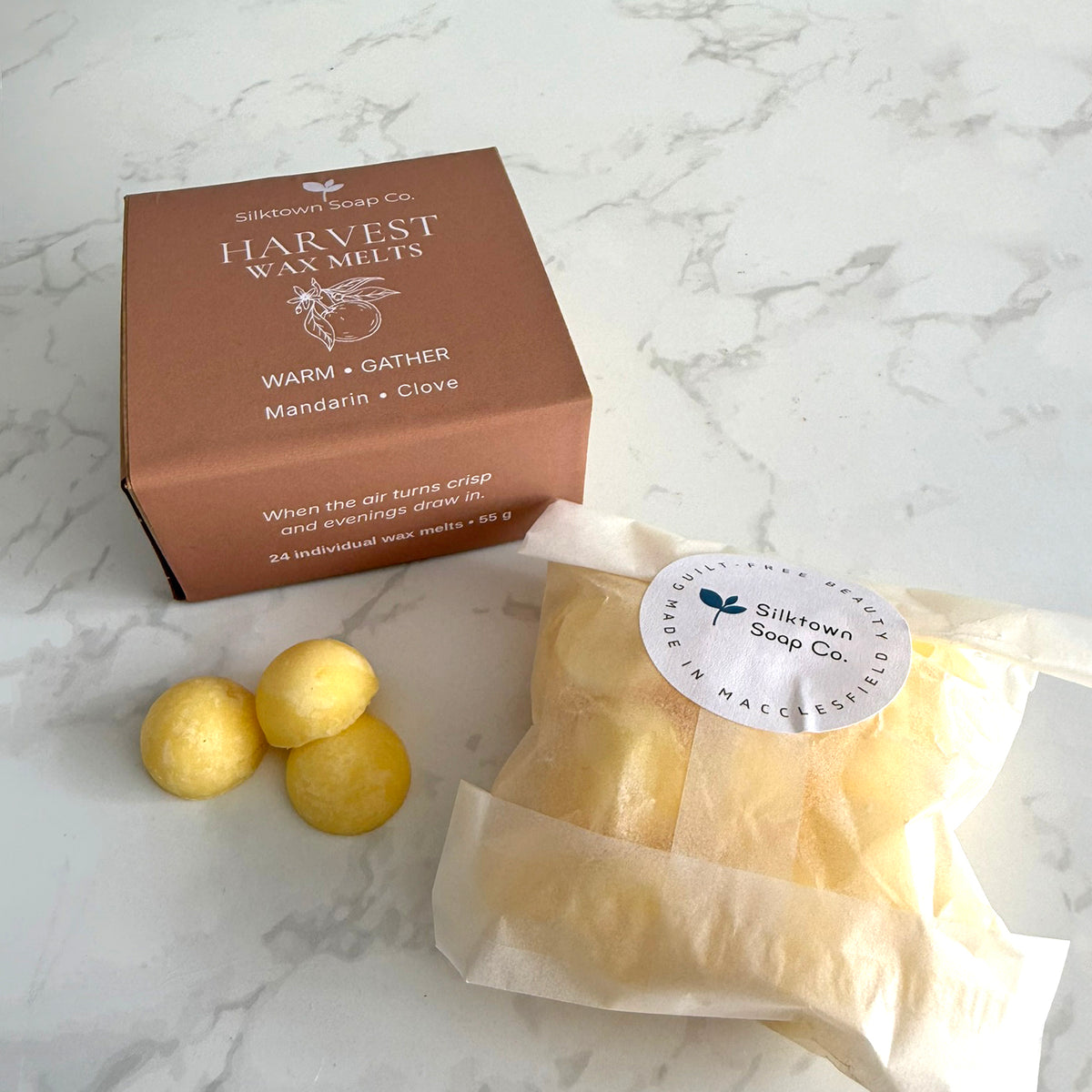 Silktown Soap Co. Harvest Wax Melts package set on a white marble surface, featuring a brown cardboard box, three yellow wax melts, and a wax melt bag with a white paper label.