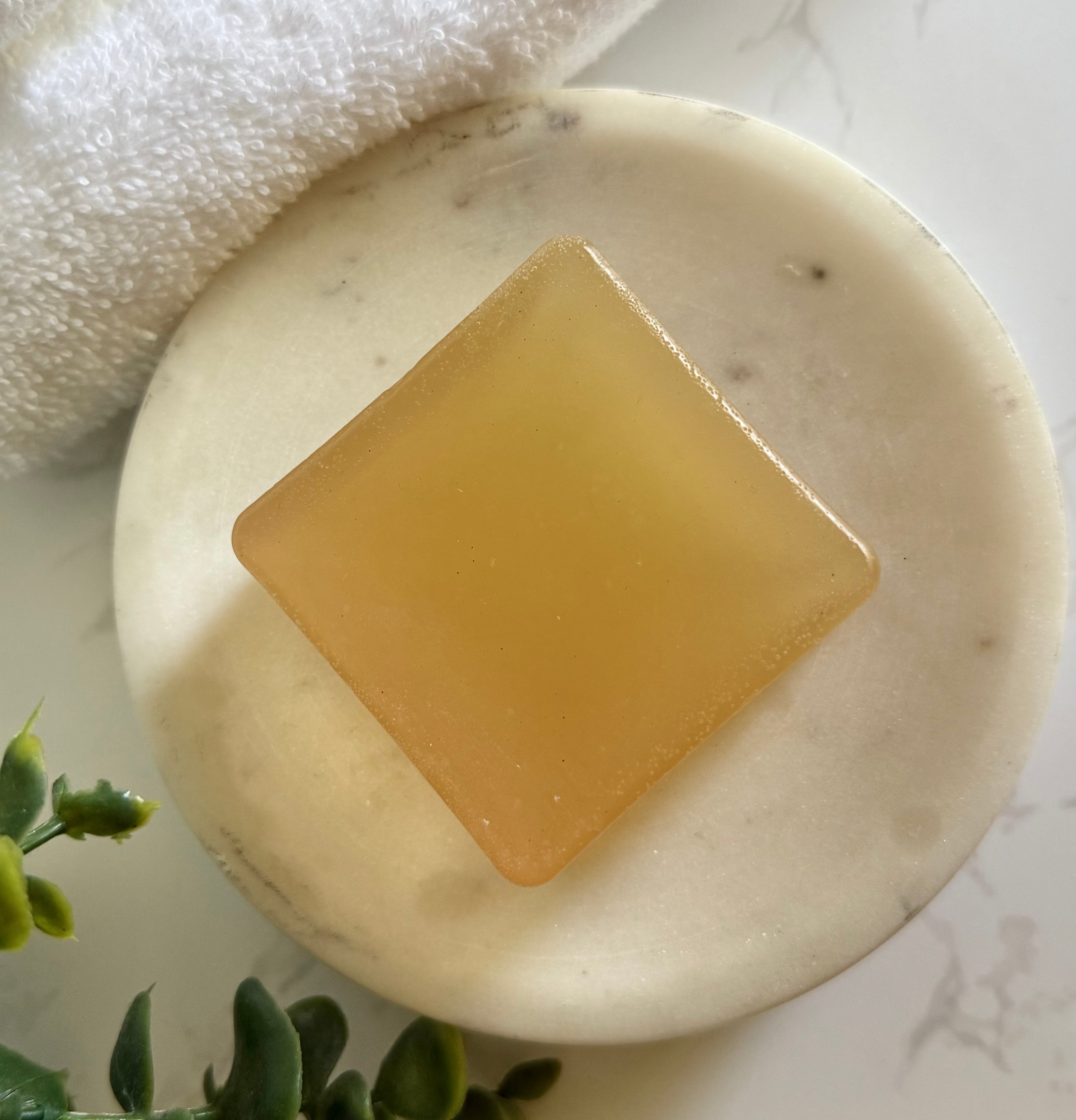 Bar of soap on a white marble surface with a towel and greenery in the background