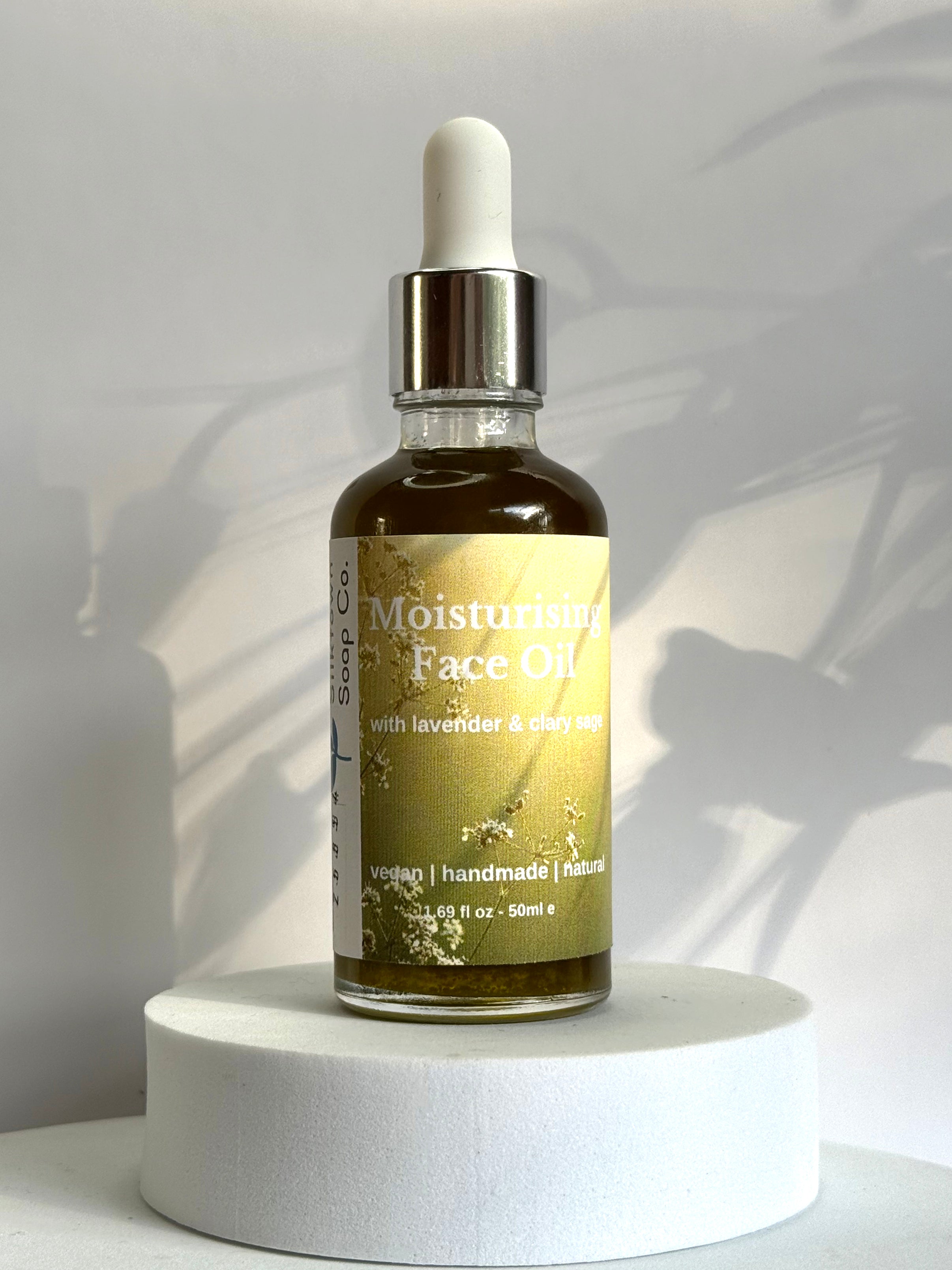 Bottle of moisturizing face oil with lavender and chamomile on a white pedestal against a light background