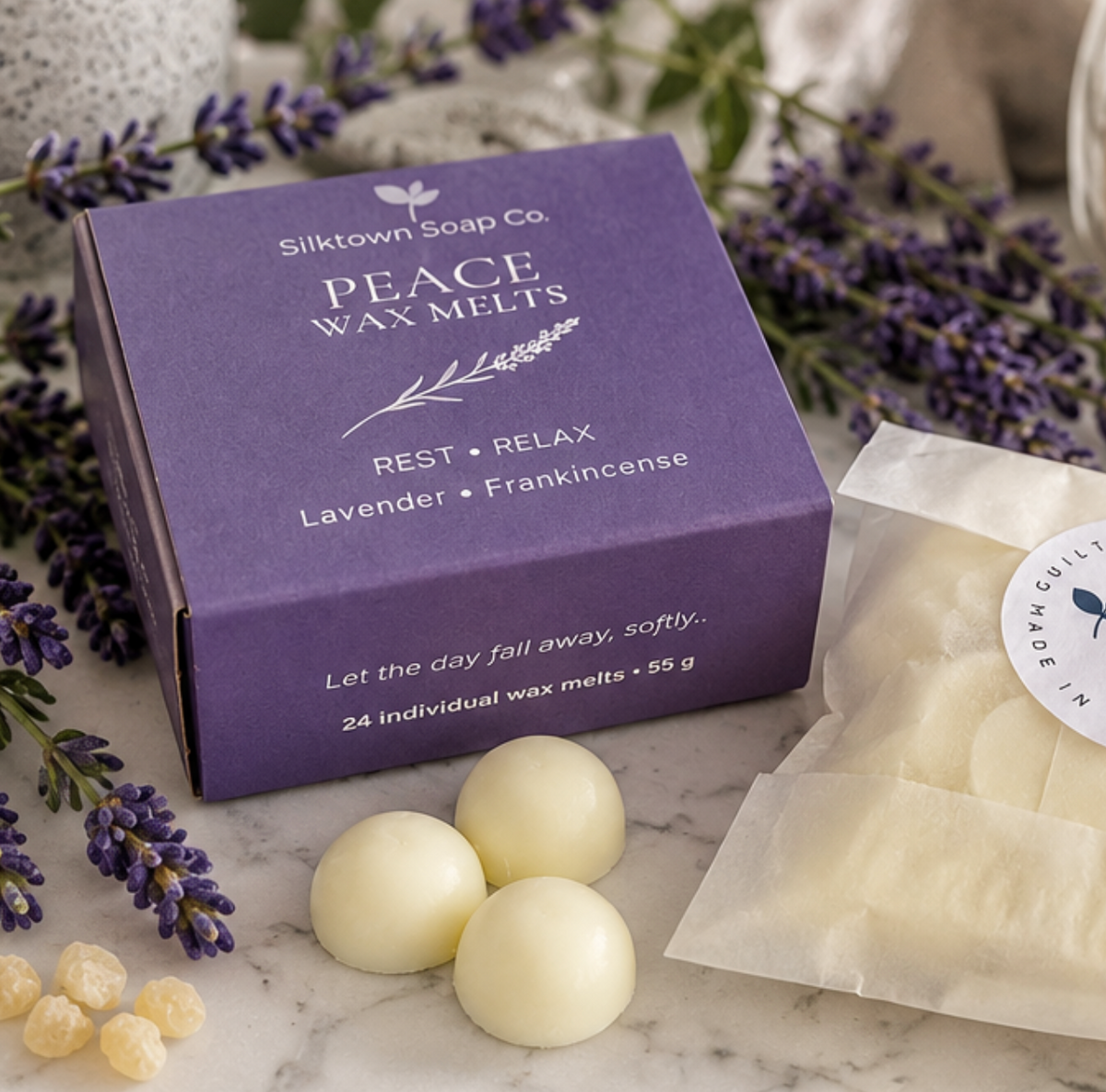 Silktown Soap Co. Peace Wax Melts lavender and frankincense box in purple packaging, shown with three white wax melts, loose wax pieces, and lavender sprigs on a marble surface.