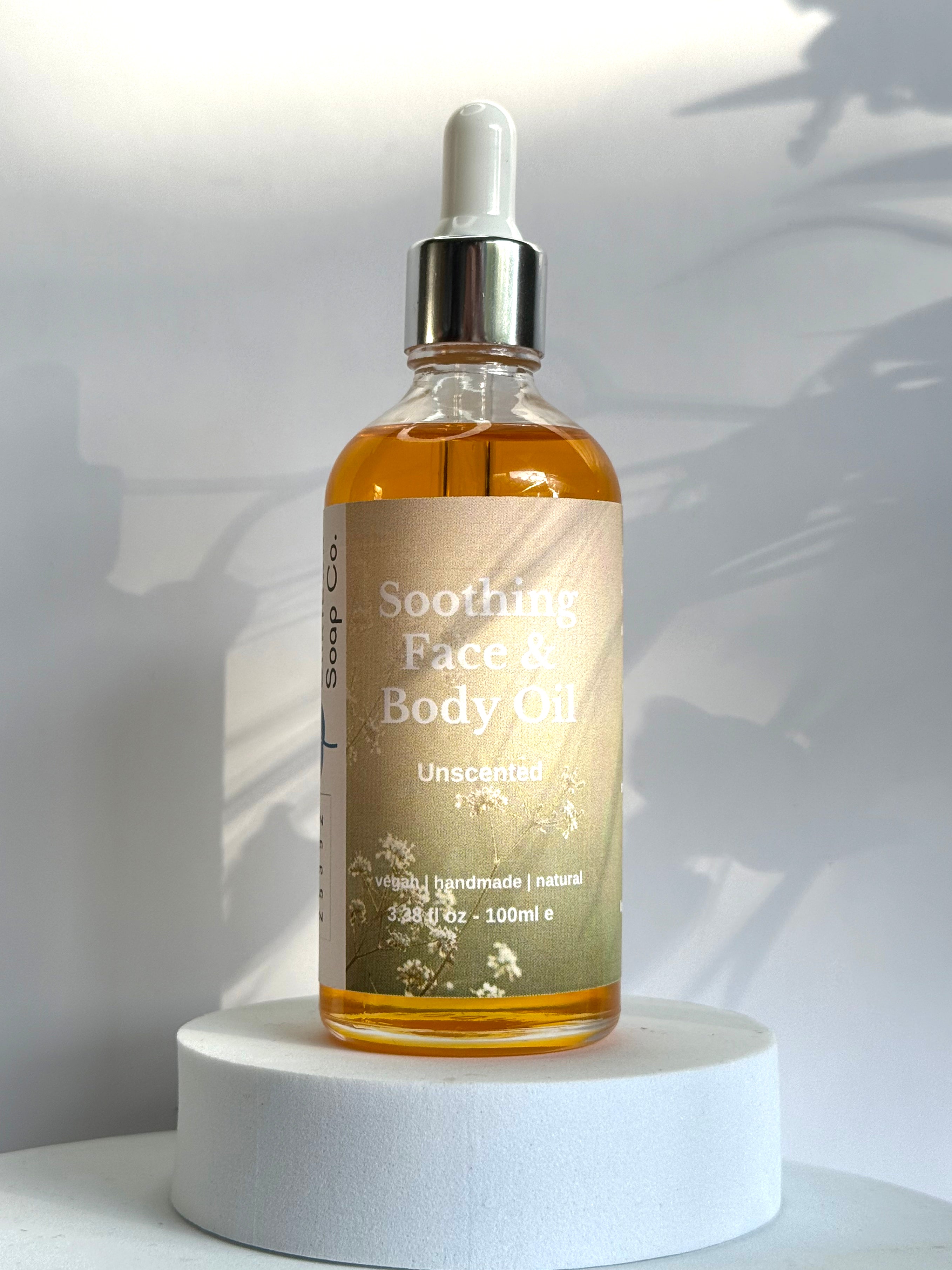 Bottle of Soothing Face & Body Oil on a white pedestal with a white background