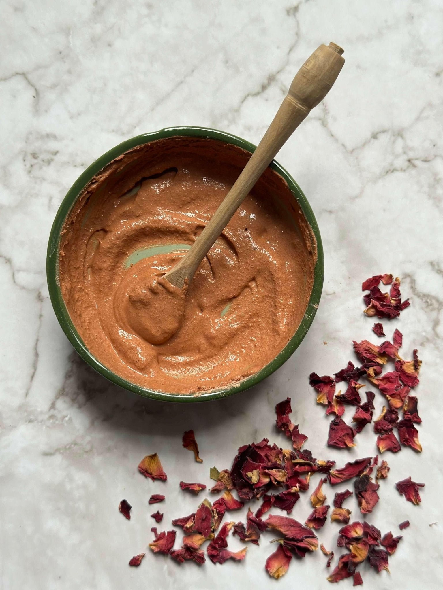 Glow Natural Clay Mask in a bowl with a wooden spoon and some rose petals after being mixed