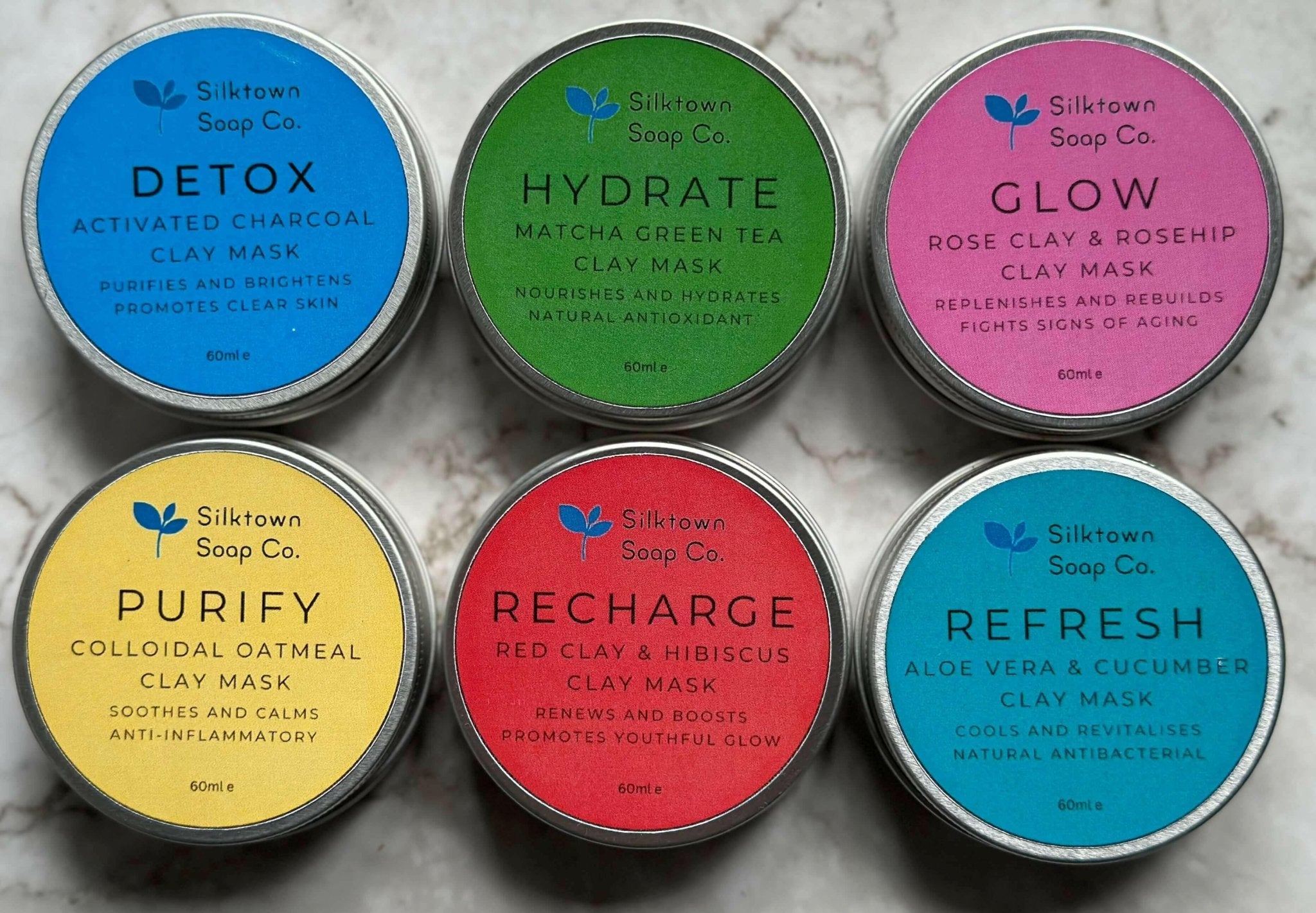 six tins of natural clay mask on a marble background