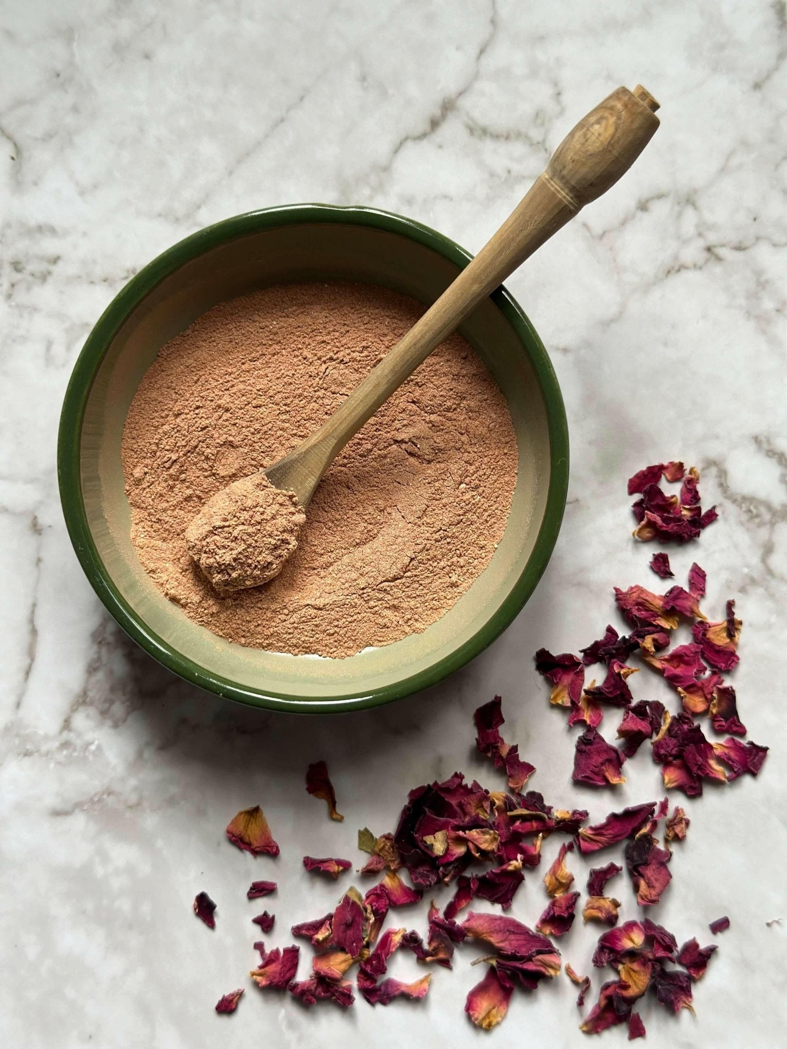 Glow Natural Clay Mask in a bowl with a wooden spoon and some rose petals before being mixed