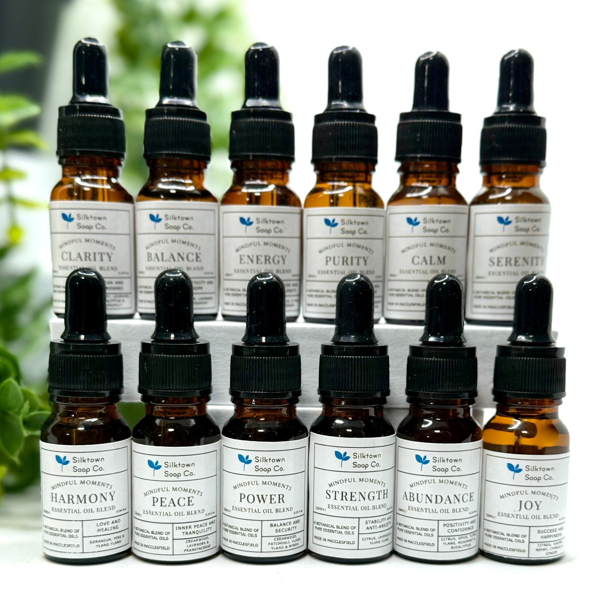 A large selection of essential oil blends in dark glass bottles with foliage in the background