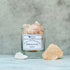 A clear glass jar on a grey background filled with pink Himalayan salt, with a label that reads &