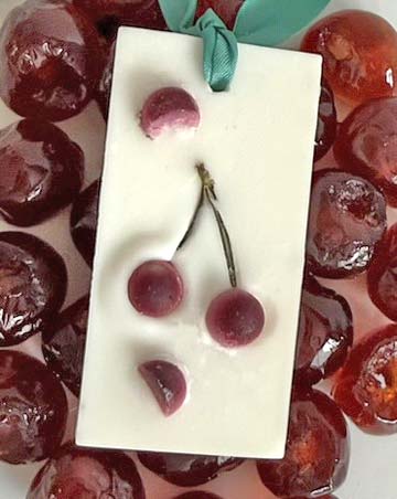 A natural wax freshener tablet with a cherry design, accompanied by real cherries and a satin ribbon for hanging.