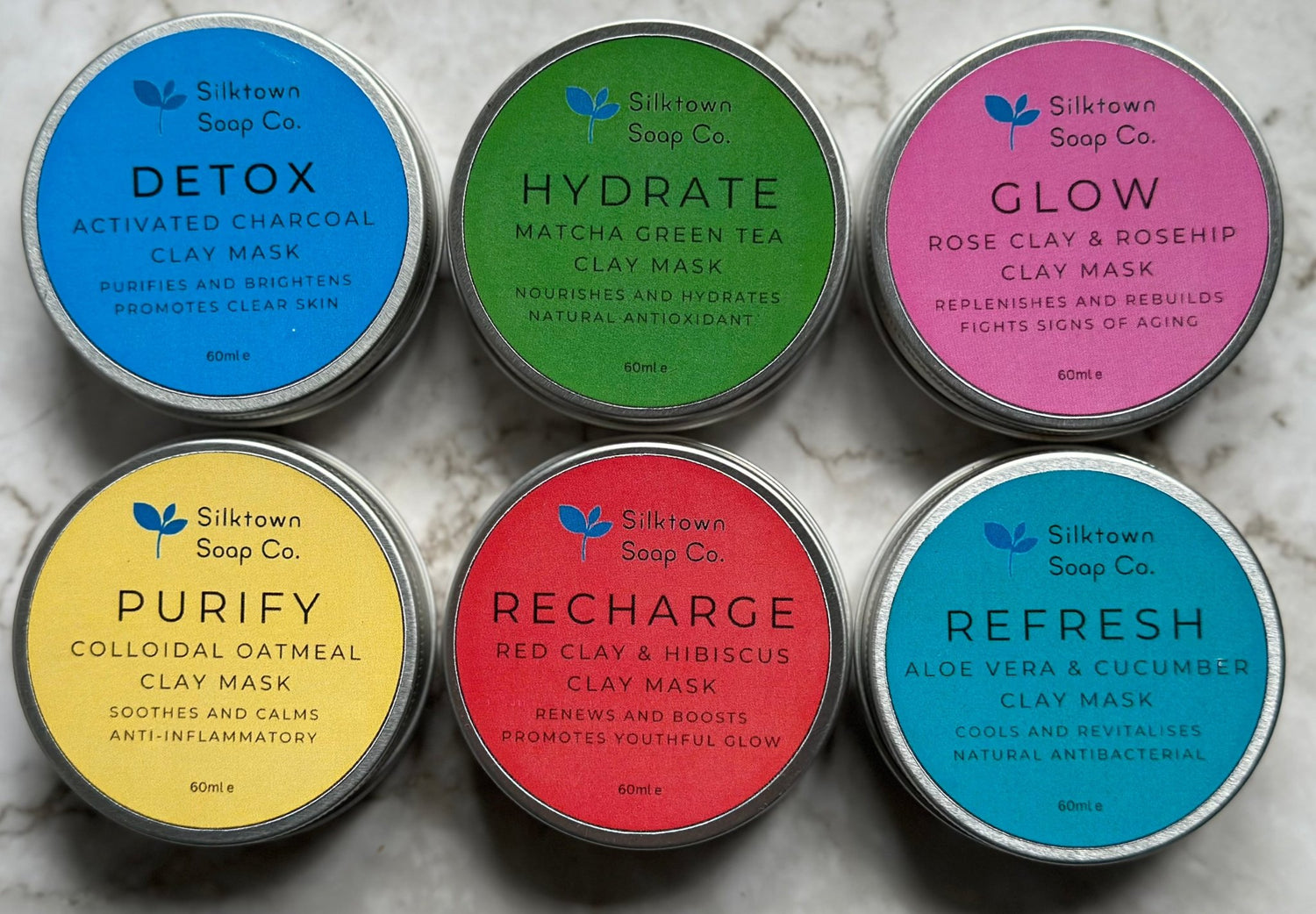 six tins of natural skincare clay face masks on amarble background