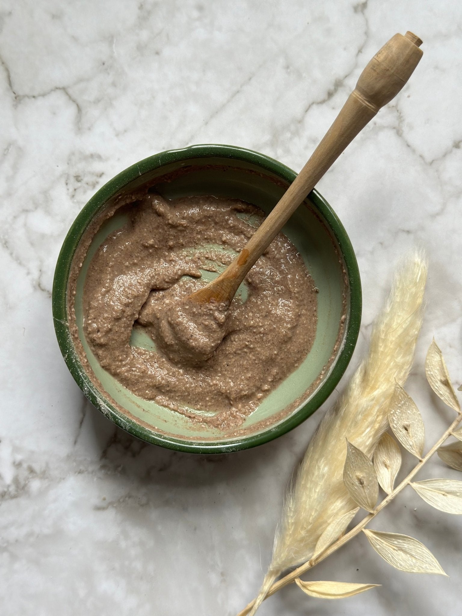Purify Natural Clay Mask in a bowl with a wooden spoon and some foliage after  being mixed