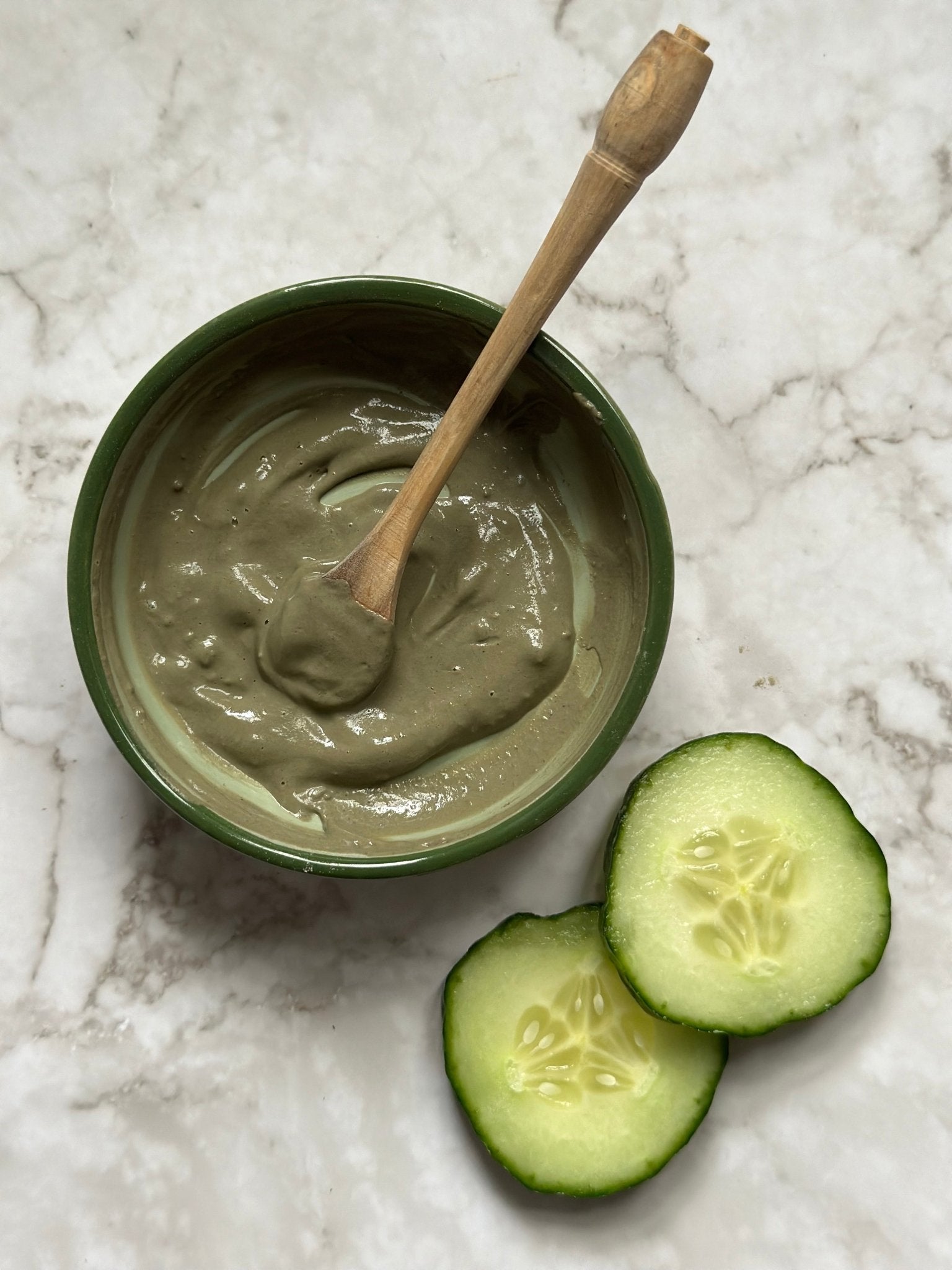 Refresh Natural Clay Mask in a bowl with a wooden spoon and some fresh cucumber slices after being mixed