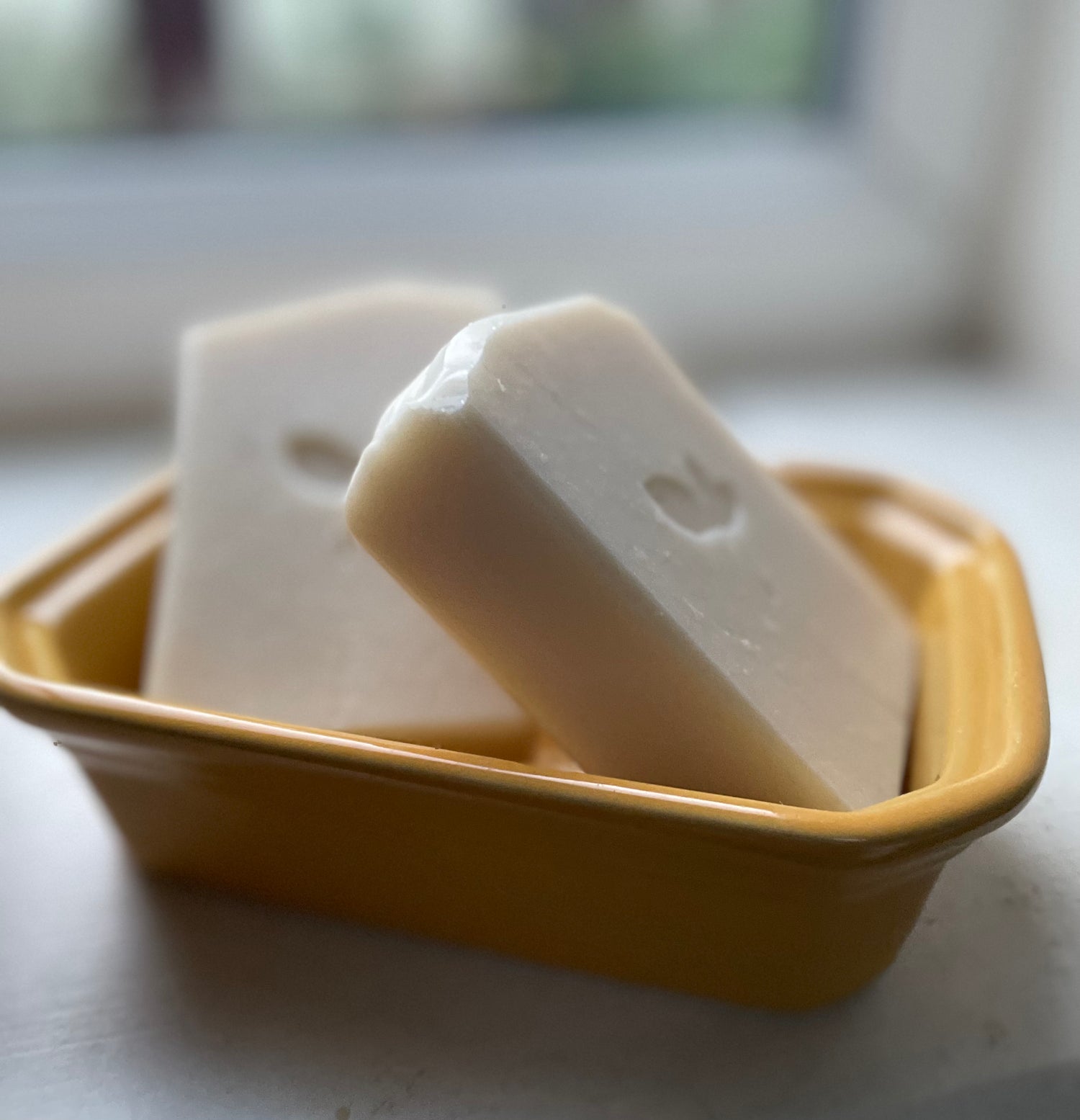 Two handmade soap bars in a dish on the windowsill