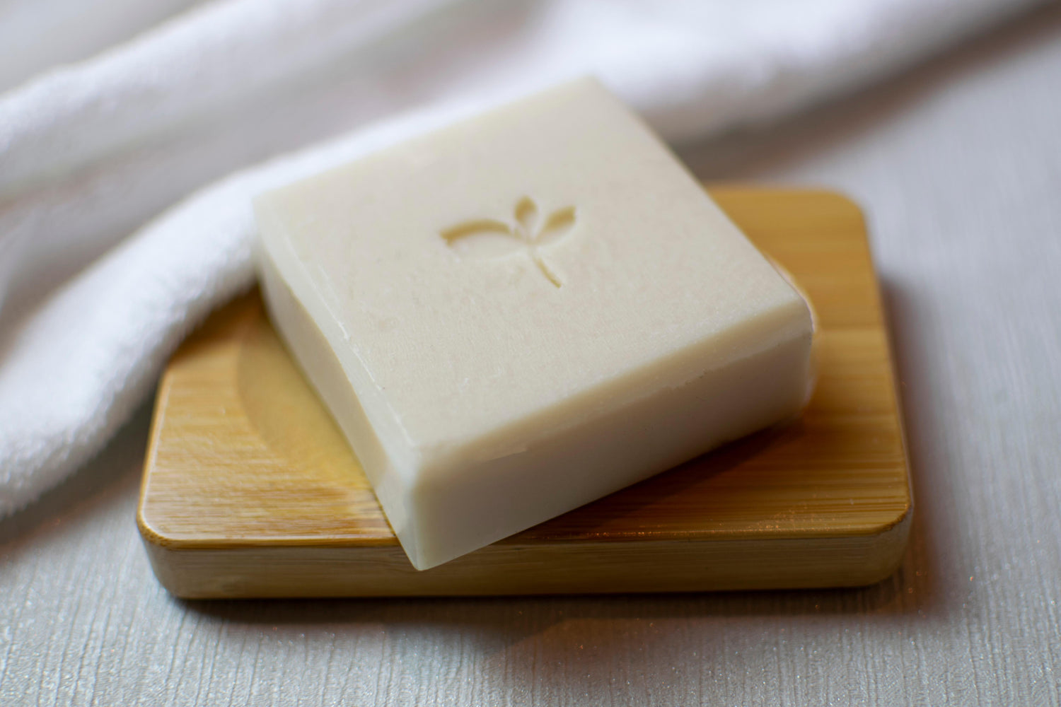Natural soap bar on a bamboo soap dish with a white towel