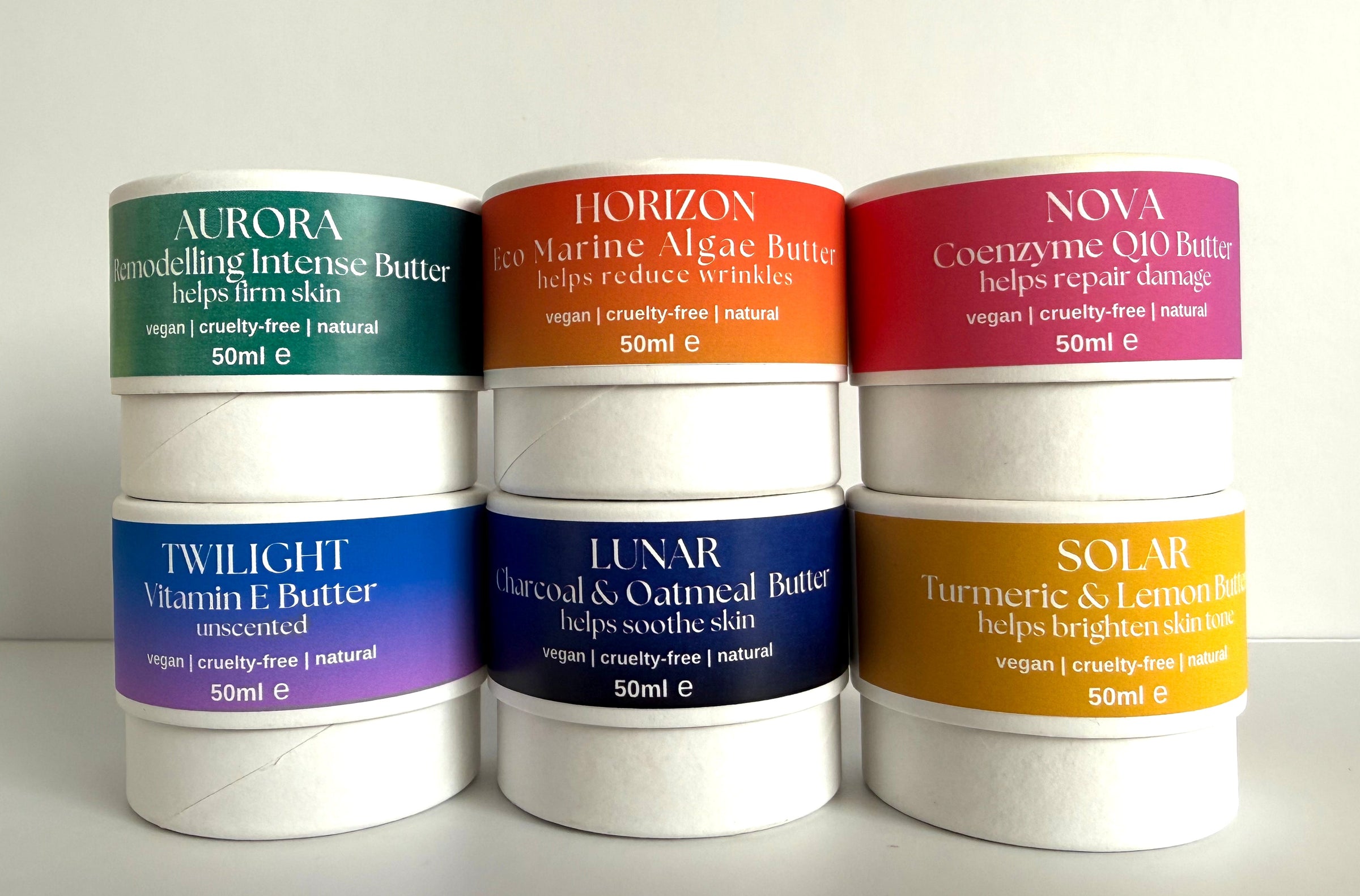 Natural Skincare butters in white pots with colourful labels stacked on a light background