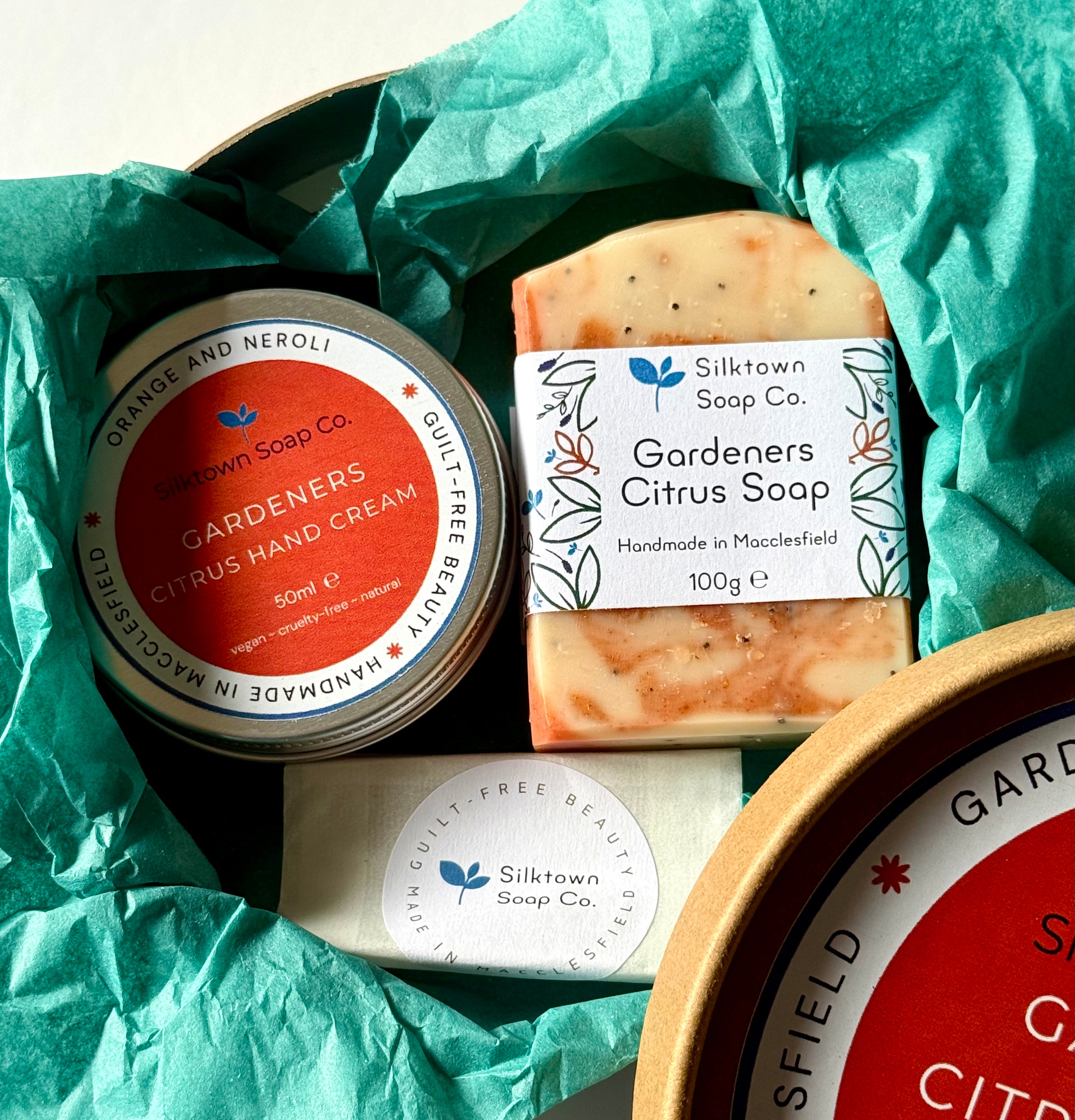 Silktown Soap Co. Natural Skincare products including a tin of hand cream and a bar of soap on teal tissue paper.