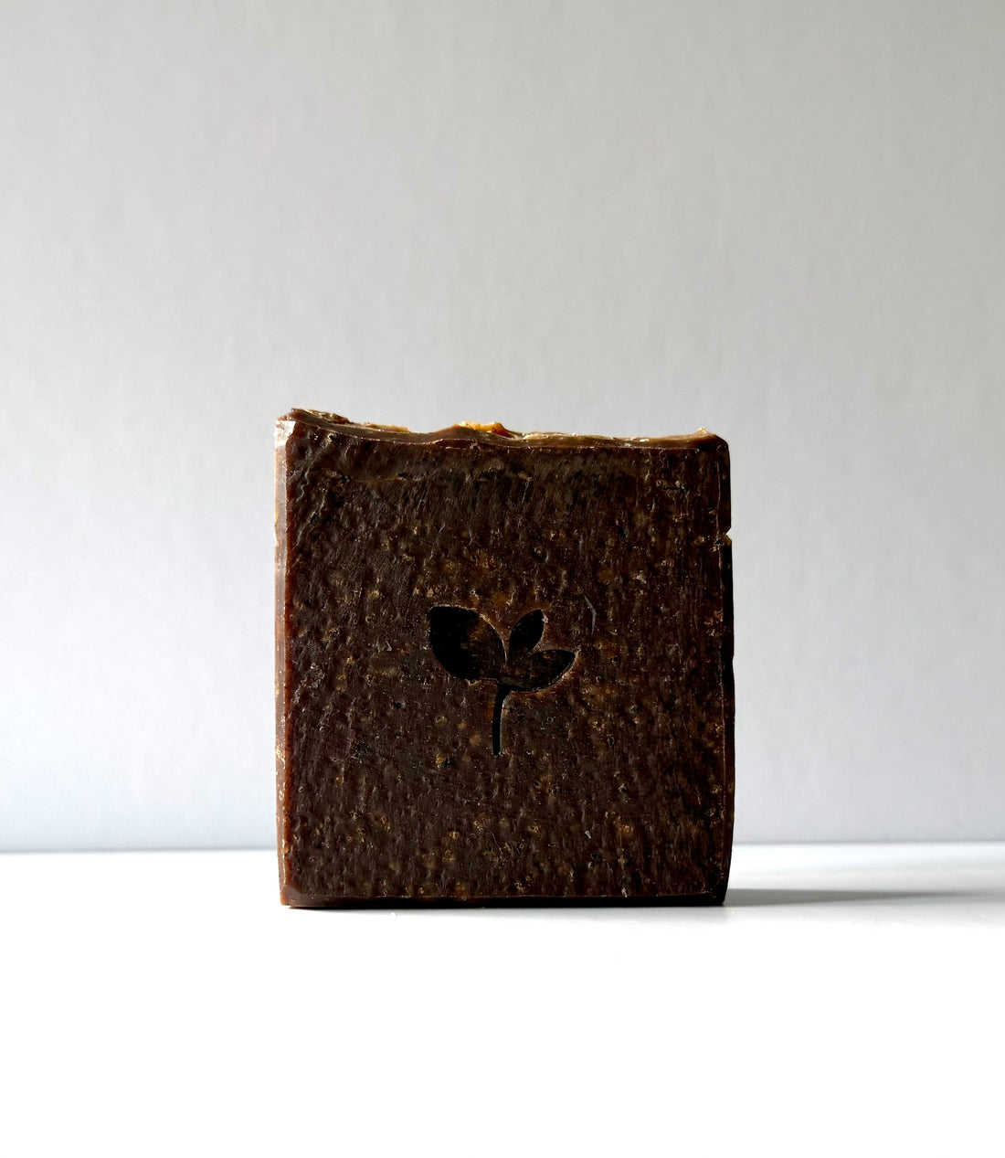 Bar of dark natural soap with a logo on a white background