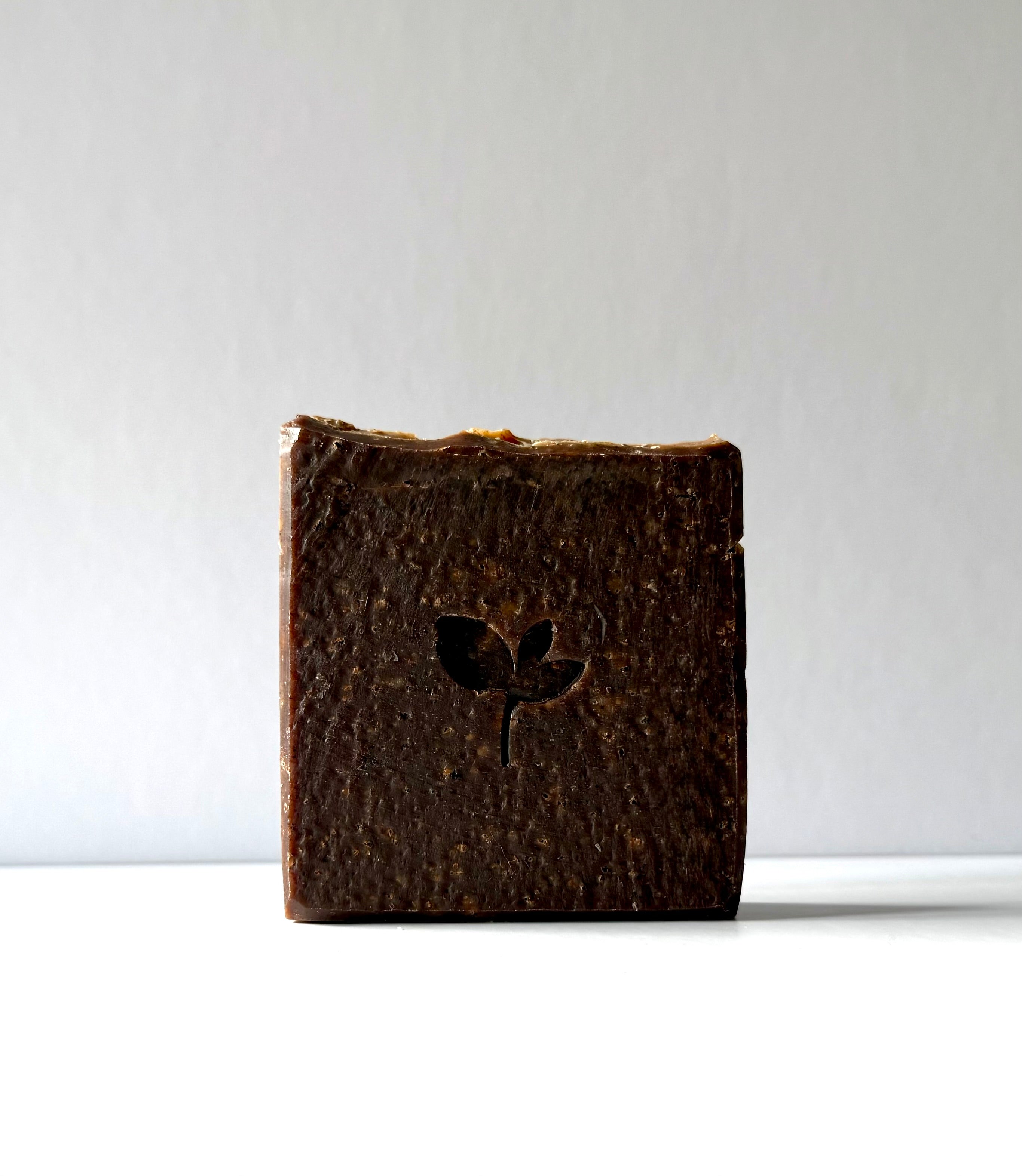 Bar of dark natural soap with a logo on a white background