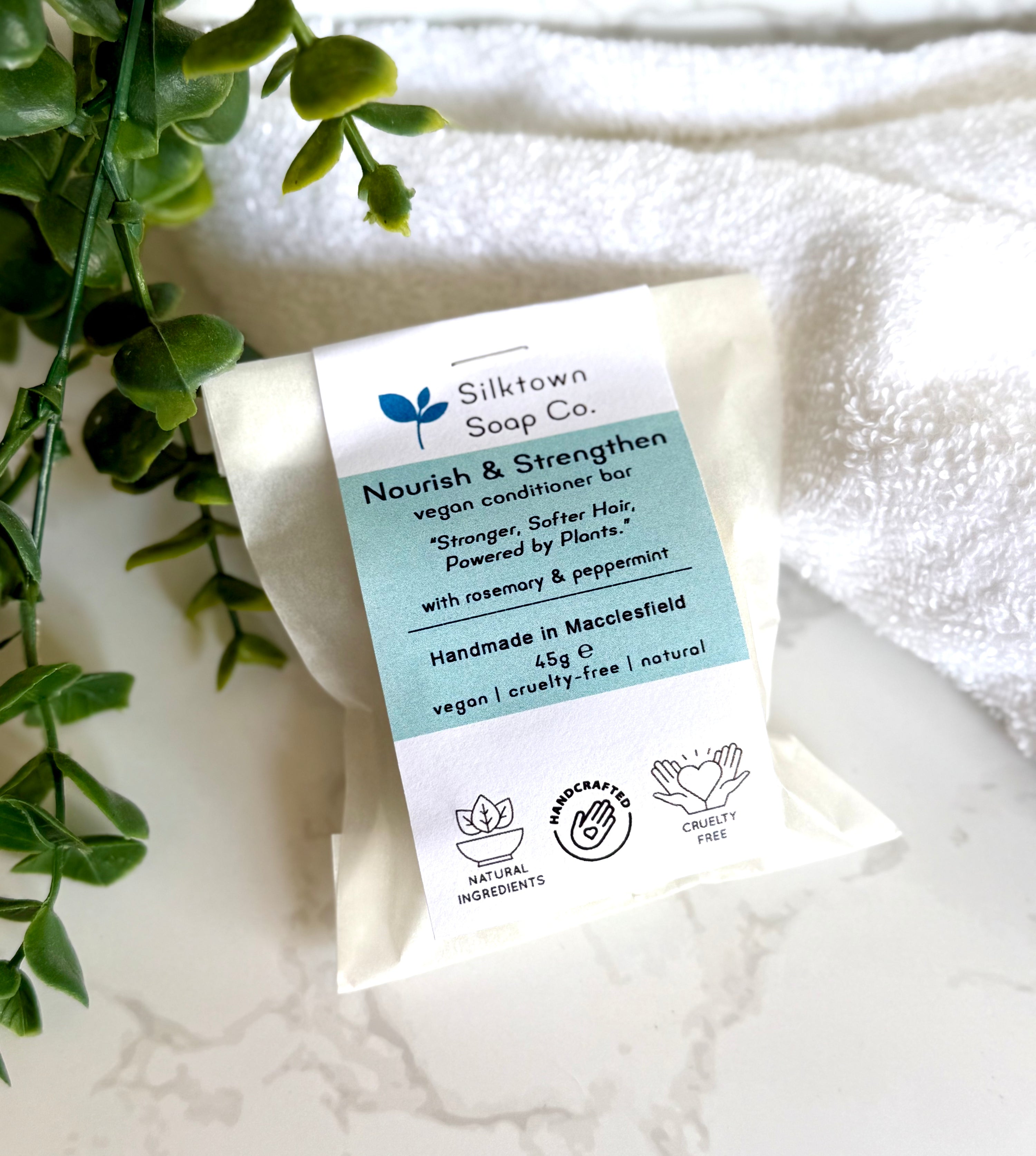Nourish &amp; Stregthen Natural Haircare Conditioner Bar in packaging with a towel and foliage