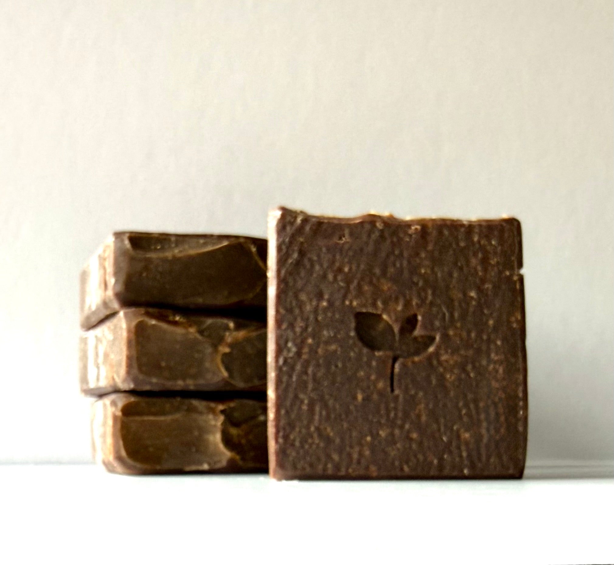 Three bars of dark natural soap with a leaf design on a light background