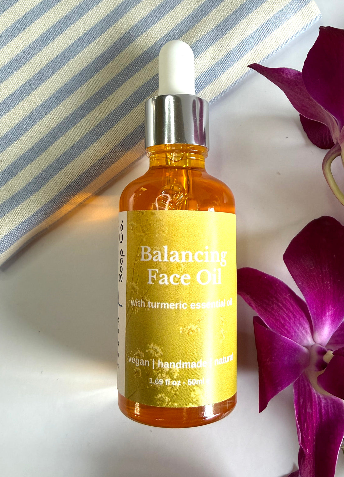 Balancing Face Oil bottle with turmeric essence on a striped background with flowers.