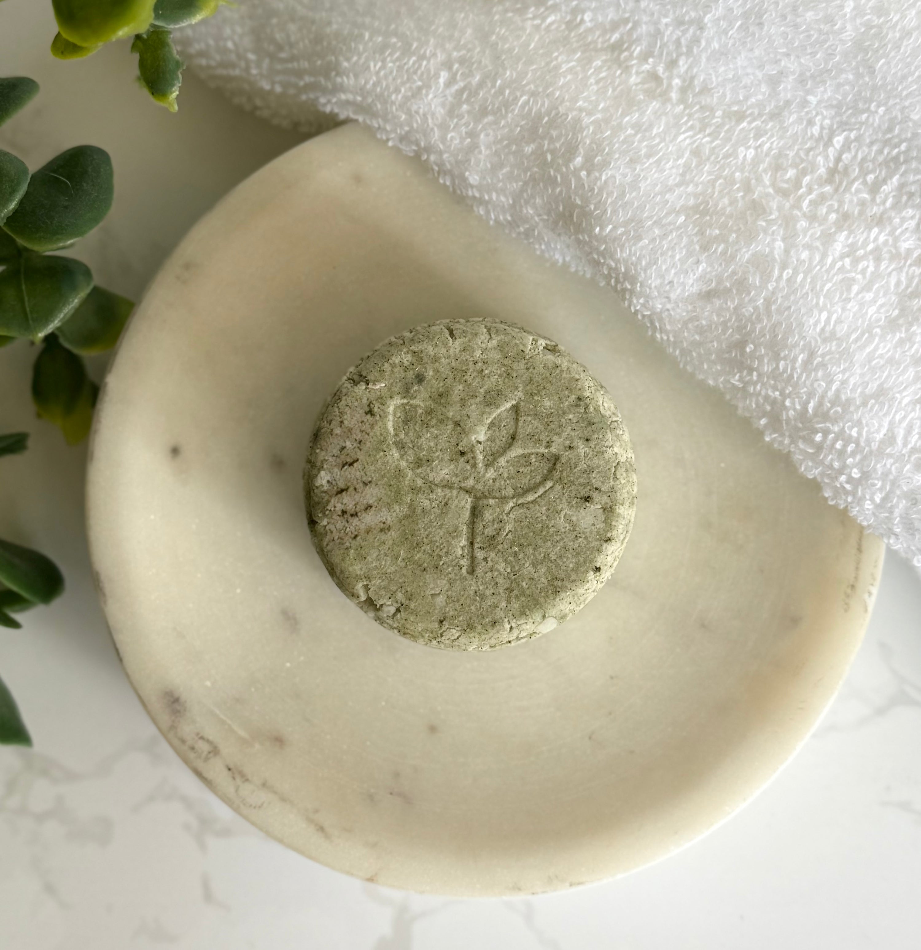 Natural Shampoo Bar - Balancing Act with leaf design on a white marble surface with a white towel and green leaves.
