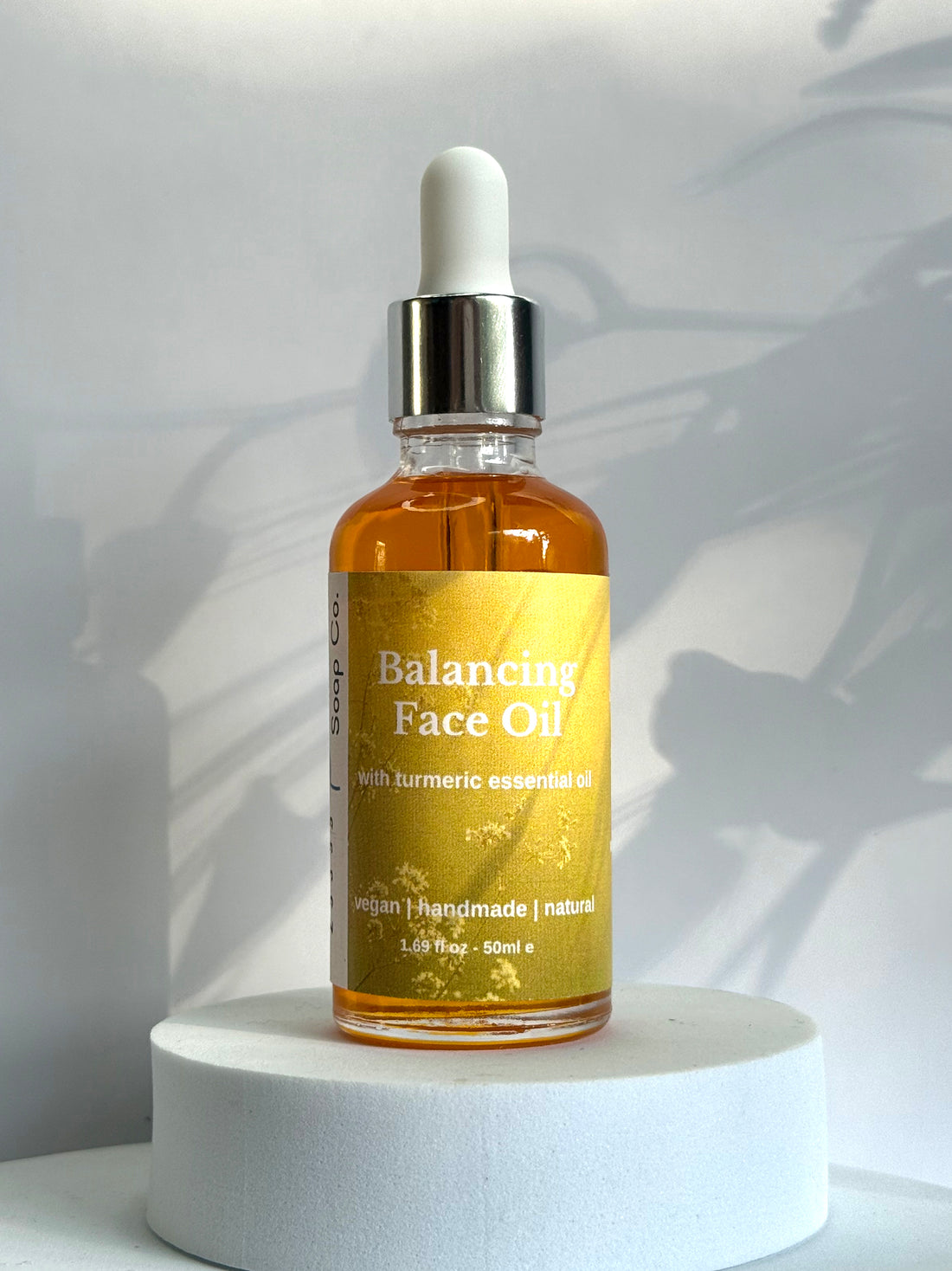 Bottle of balancing face oil on a white pedestal with a neutral background