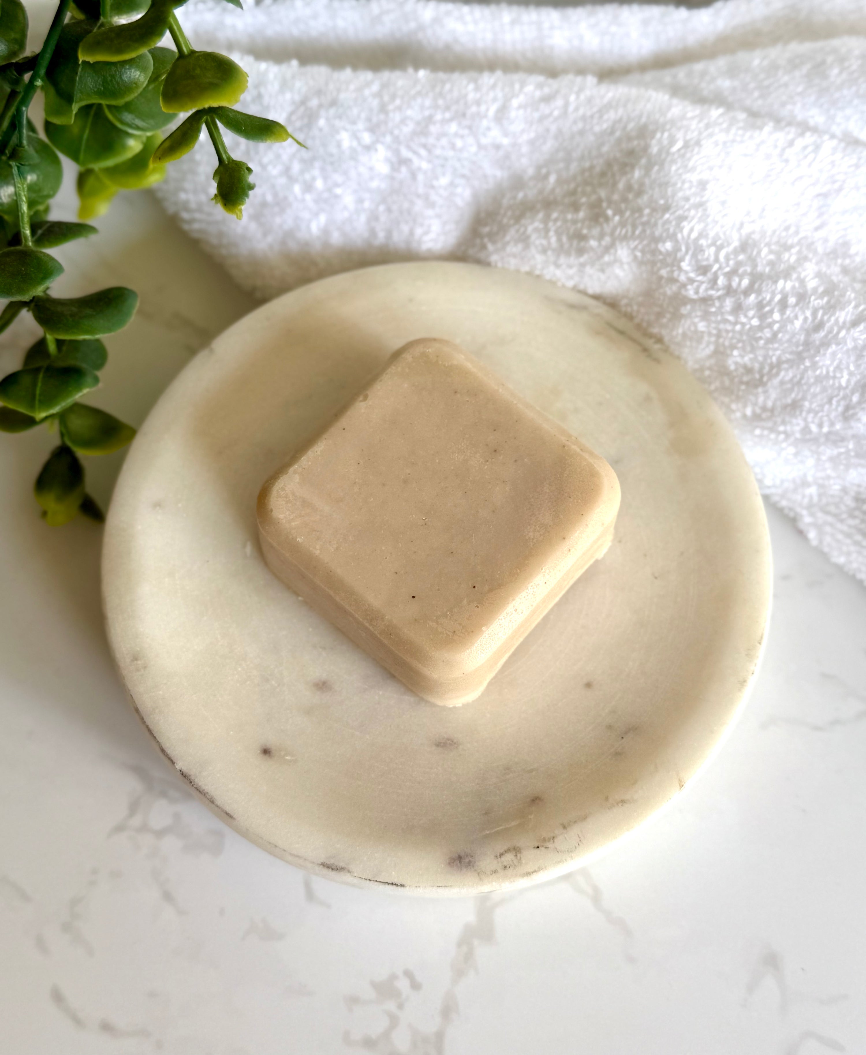 Calm &amp; Shine Natural Haircare Conditioner Bar on a marble dish with a towel and foliage