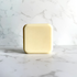 A single pale yellow rectangular bar of conditioner with rounded corners, standing upright on a white marble surface against a matching marble background.