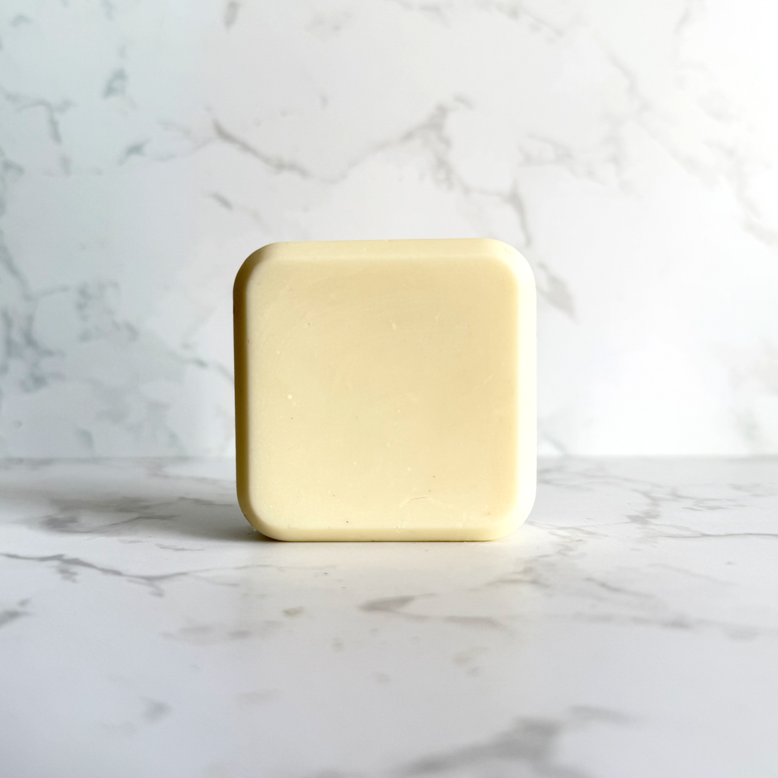 A single pale yellow rectangular bar of conditioner with rounded corners, standing upright on a white marble surface against a matching marble background.