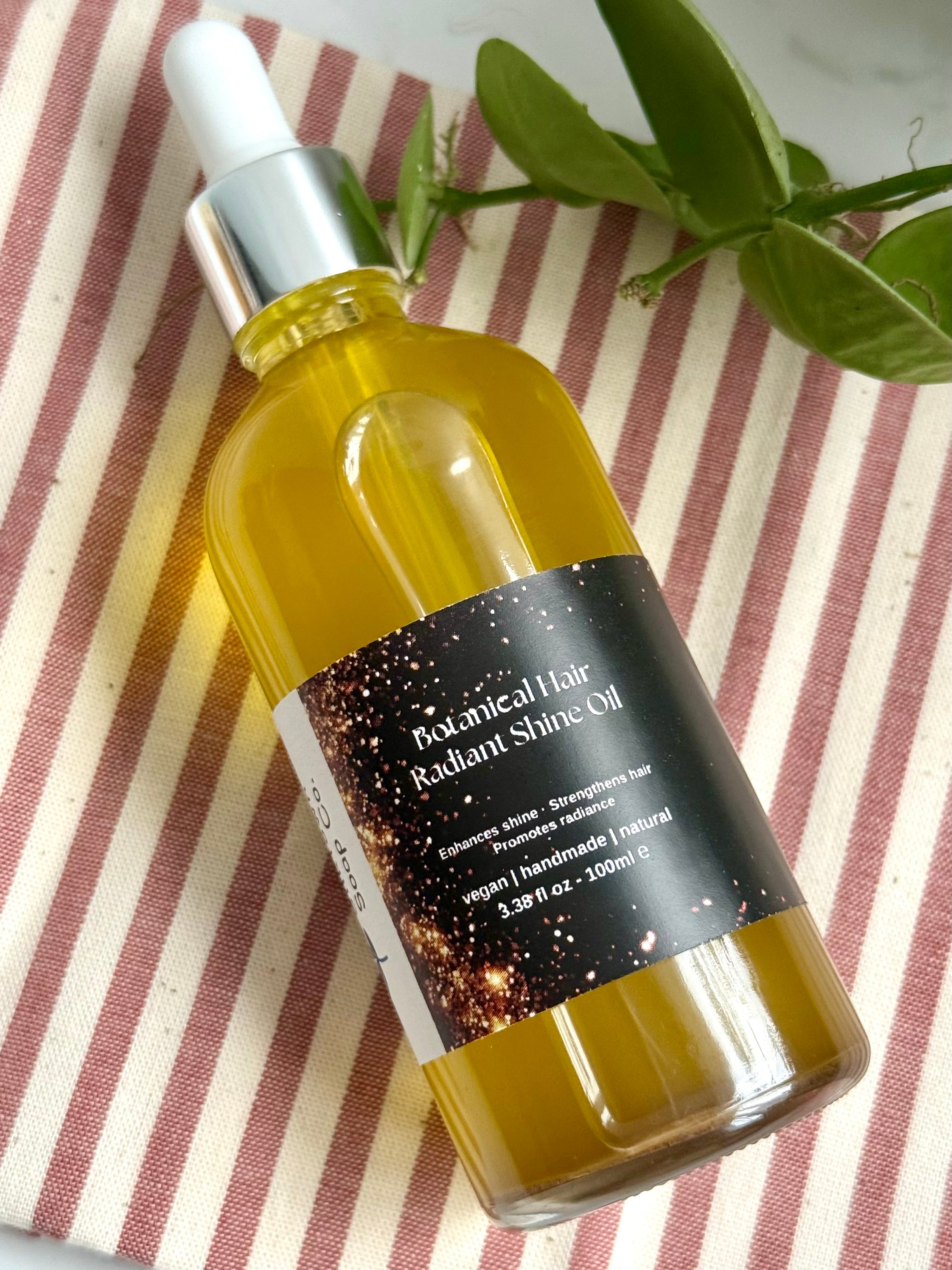 Bottle of Botanical Hair Radiant Shine Oil on a striped fabric background