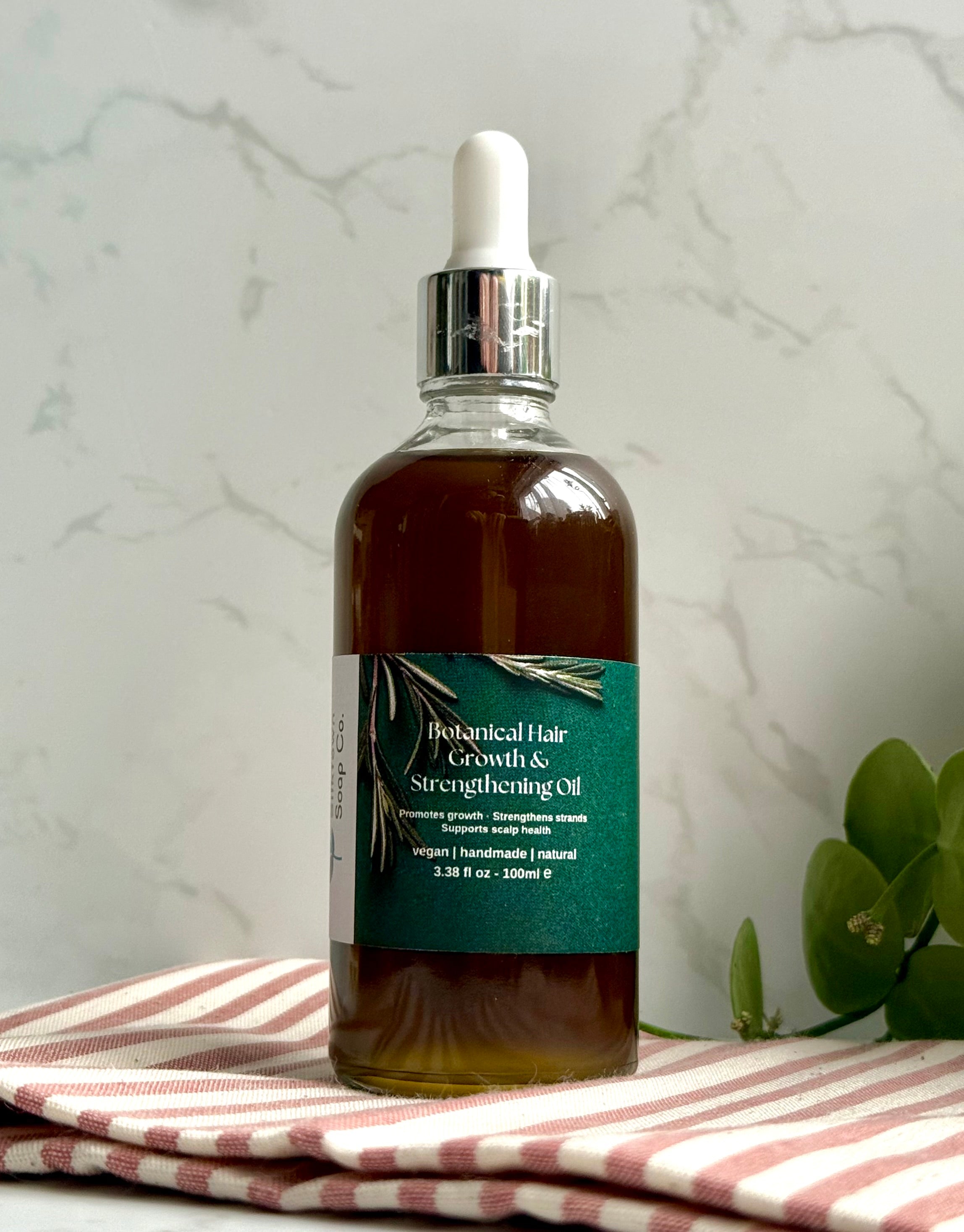 Bottle of botanical hair growth oil on a striped cloth with a marble background