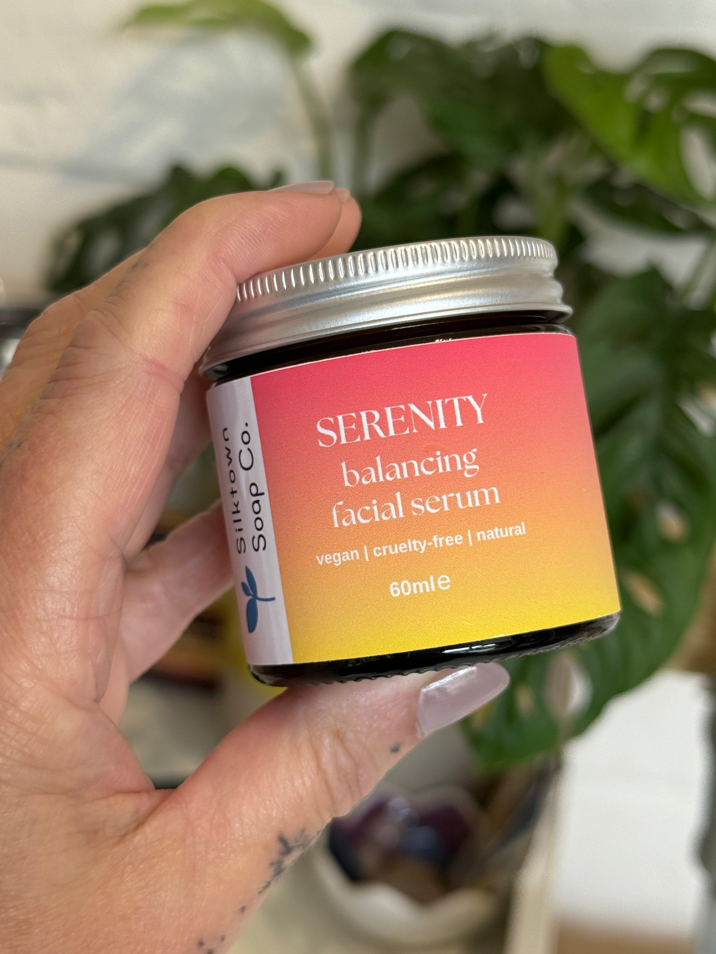 Hand holding a jar of Serenity Balancing Natural Facial Serum with a blurred background