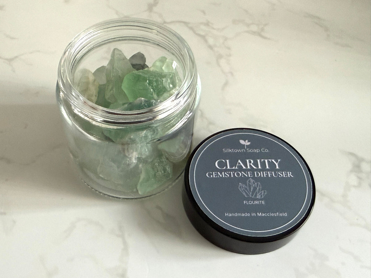 A clear glass jar filled with pale green gemstone pieces sits beside a black round lid labeled &
