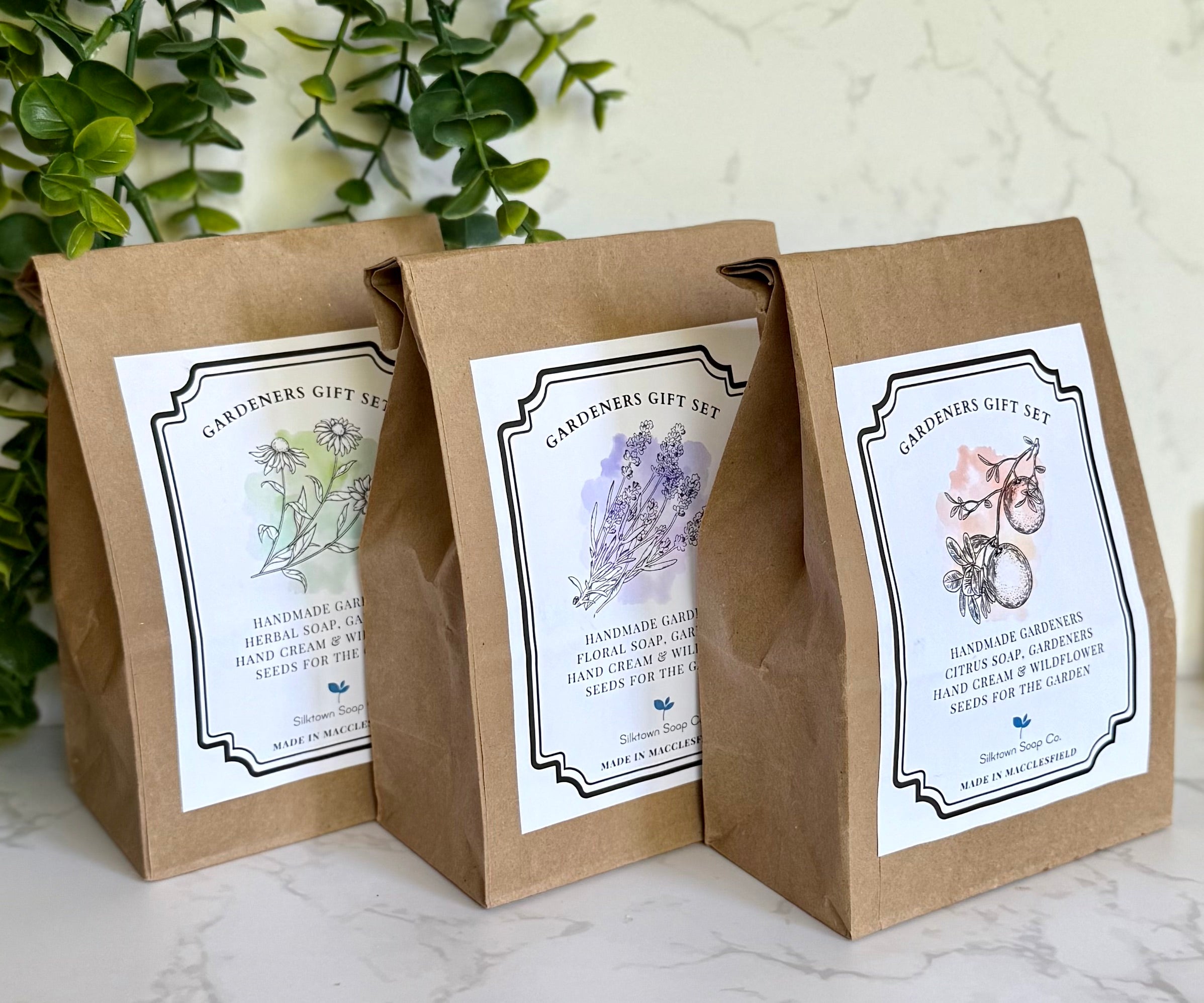 Three brown paper bags with white labels featuring gardening-themed designs on a marble surface.