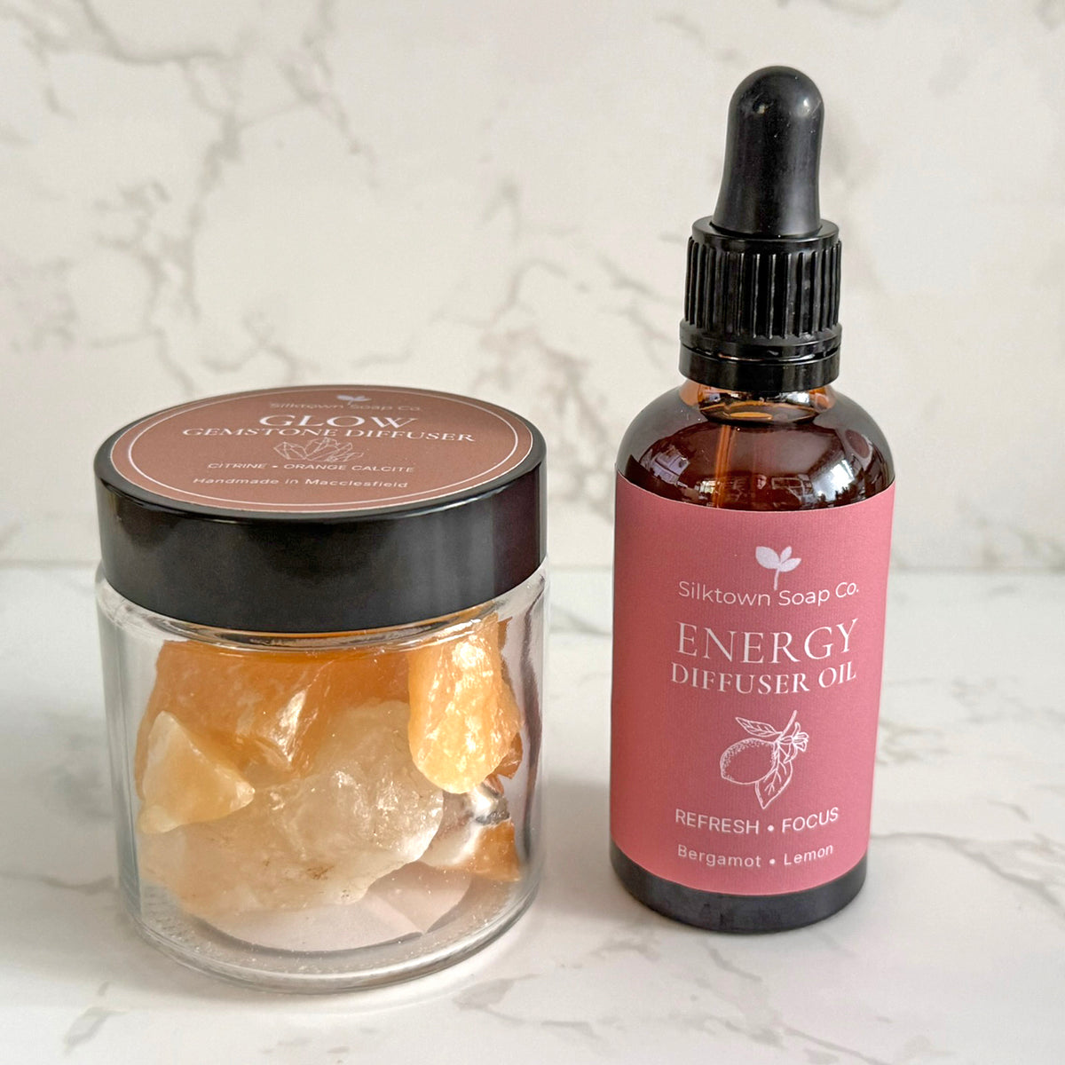 A clear glass jar filled with orange crystal stones next to a dark amber dropper bottle labeled &