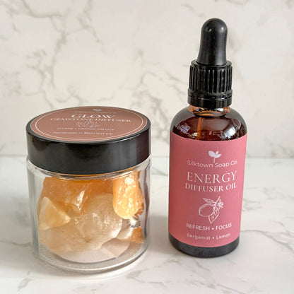 A clear glass jar filled with orange crystal stones next to a dark amber dropper bottle labeled &