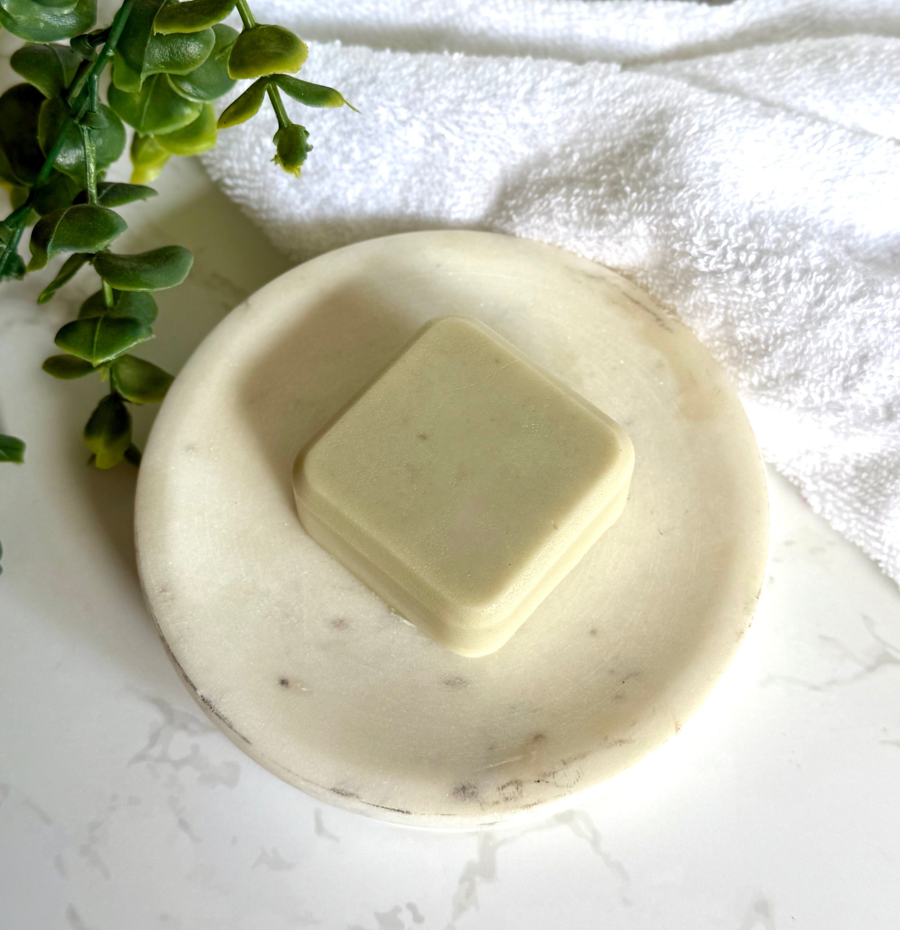 Rosemary &amp; Peppermint Natural Conditioner Bar on a marble dish with a towel and foliage