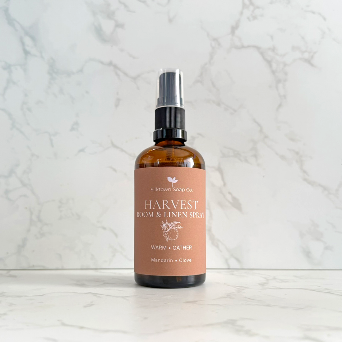 Silktown Soap Co. Harvest Room &amp; Linen Spray in a 16 oz amber glass bottle with a black spray nozzle and a dusty rose label, set against a white marble background.