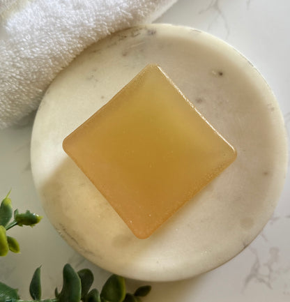 Bar of soap on a white marble surface with a towel and greenery in the background