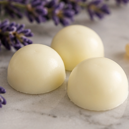 Three smooth, dome-shaped white wax melts arranged on a light marble surface with purple lavender flowers in the background.