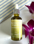 Bottle of moisturizing face oil with lavender and olive oil on a white surface with purple flowers.