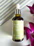 Bottle of Nourishing Face Oil with a dropper on a white surface with purple flowers.