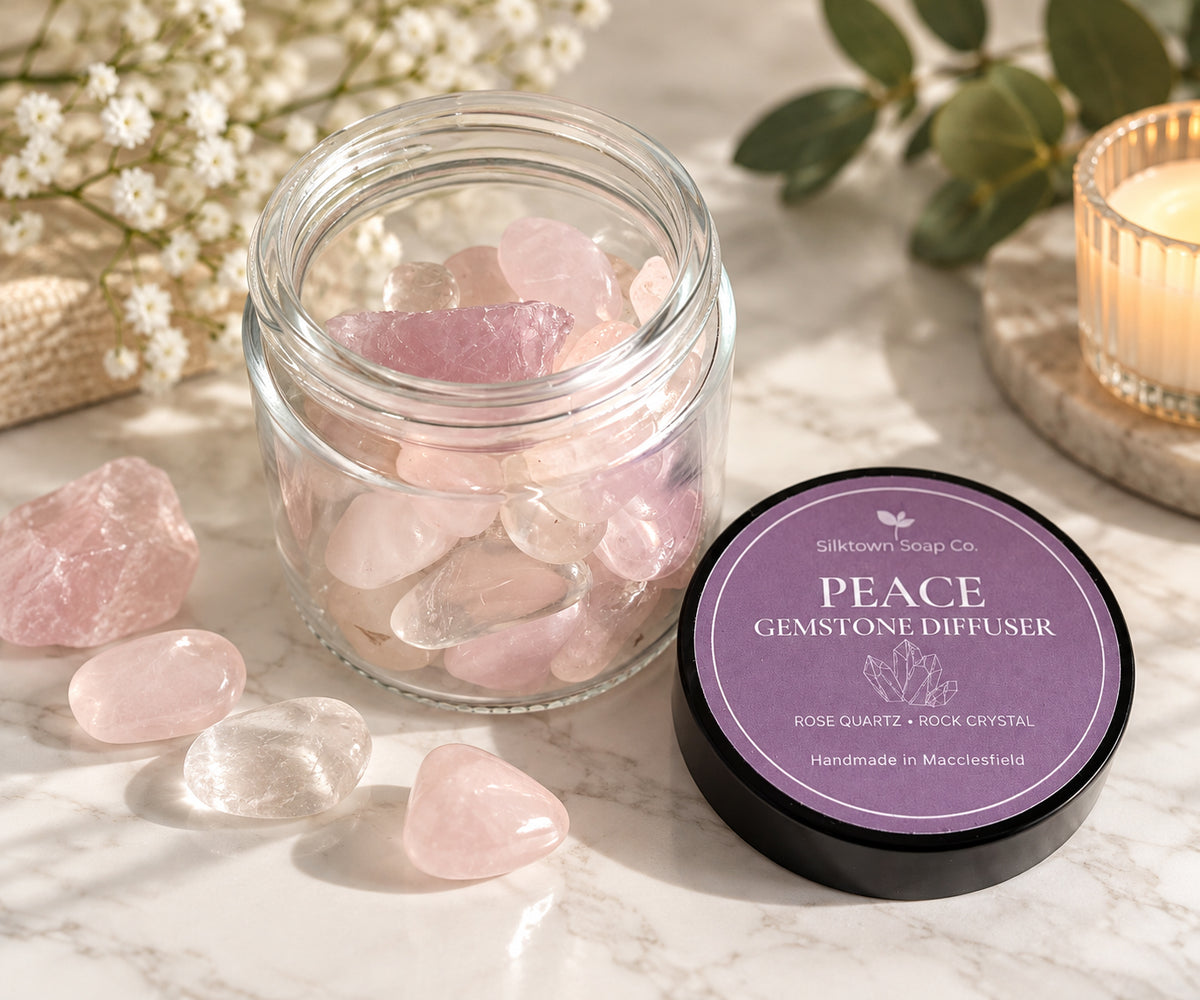 A glass jar filled with pink rose quartz gemstones sits on a marble surface beside a round black lid labeled &