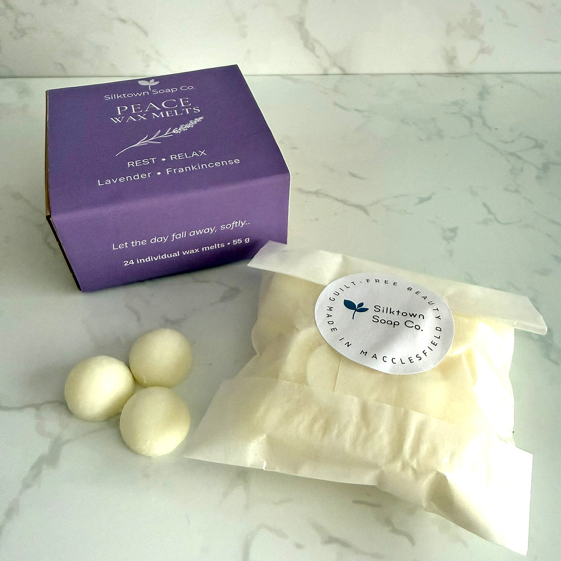 Silktown Soap Co. Peace Wax Melts set, featuring a purple cardboard box, a clear bag of cream-colored wax melts with a white circular label, and three finished wax melts on a white marble surface.