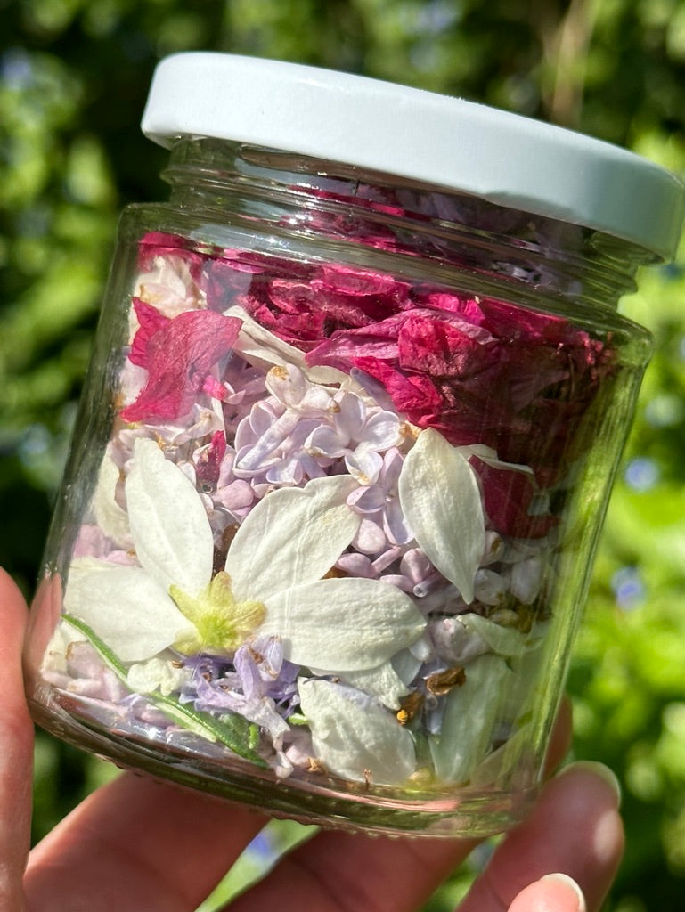 Glass jar filled with dried flowers held against a blurred green background