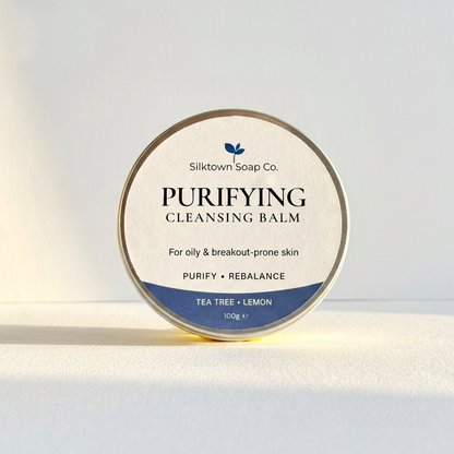 A round tin of Silktown Soap Co. Purifying Cleansing Balm (Tea Tree + Lemon) on a white surface with soft sunlight and shadows.