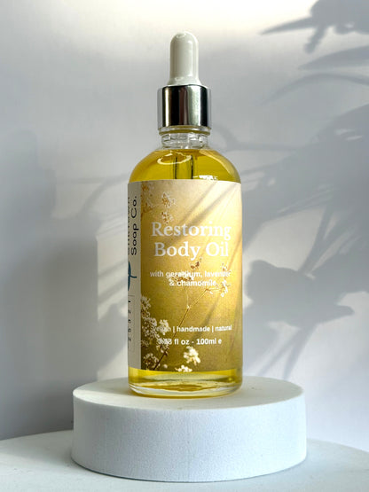 Bottle of Restoring Body Oil on a white pedestal with a white background