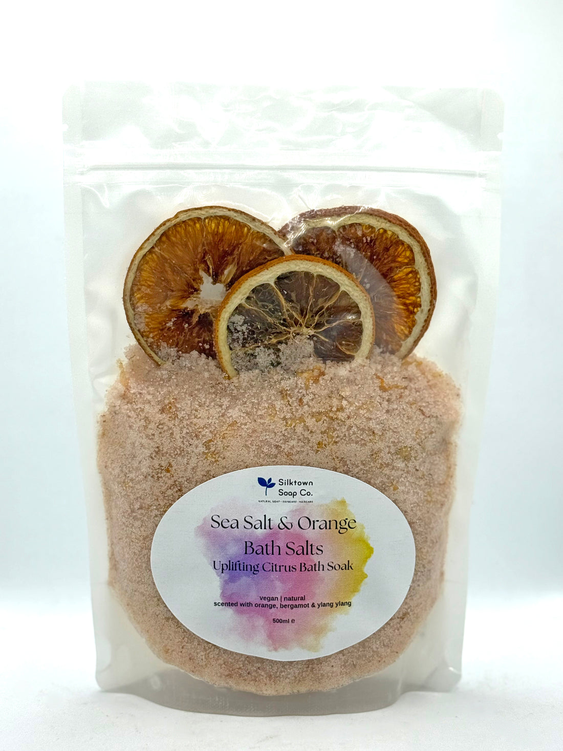 Packaged sea salt and orange bath salts with dried lemon slices on a white background